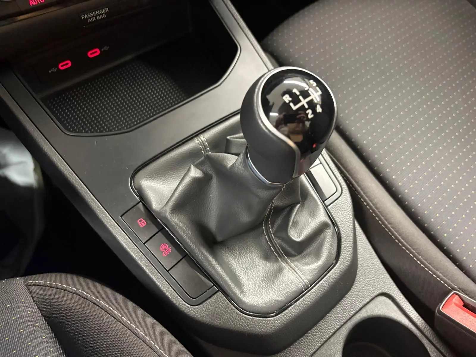 Gros plan sur le levier de vitesse manuel noir de la SEAT Ibiza gris magnétique 2024, avec console centrale et siège tissu visible.