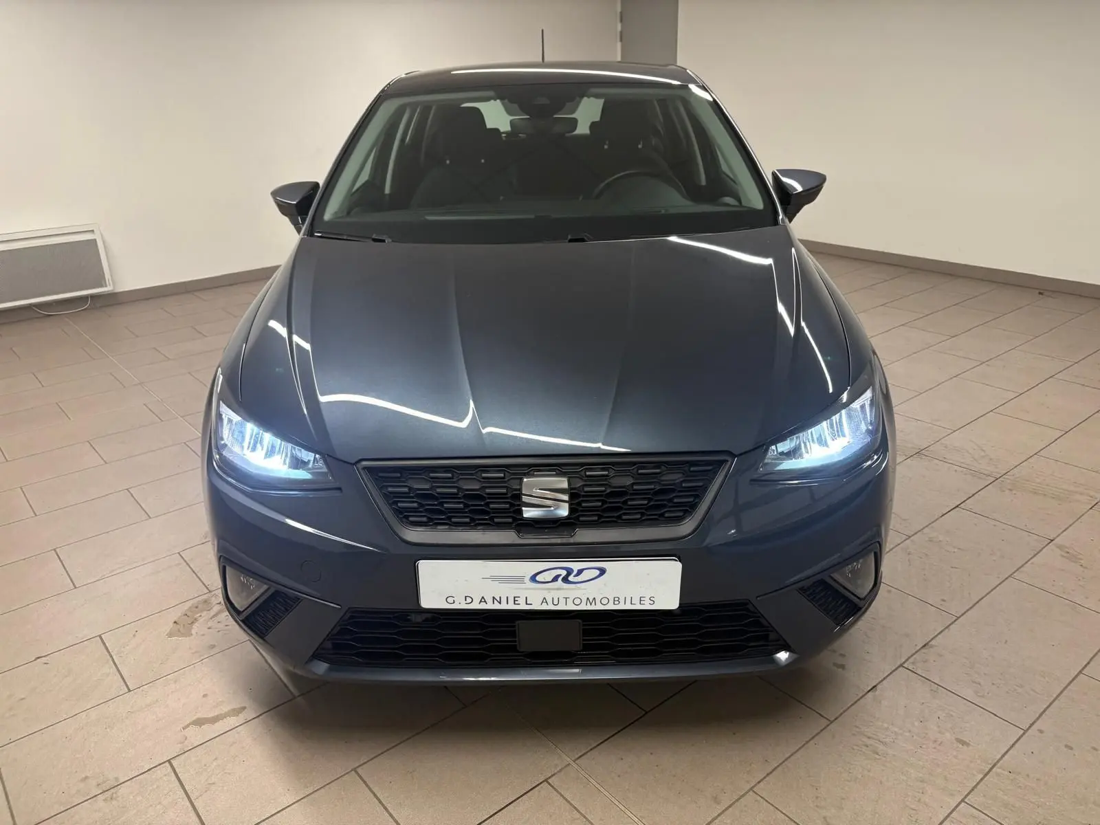 Vue frontale d'une SEAT Ibiza 2024 gris magnétique avec phares allumés dans un showroom intérieur.