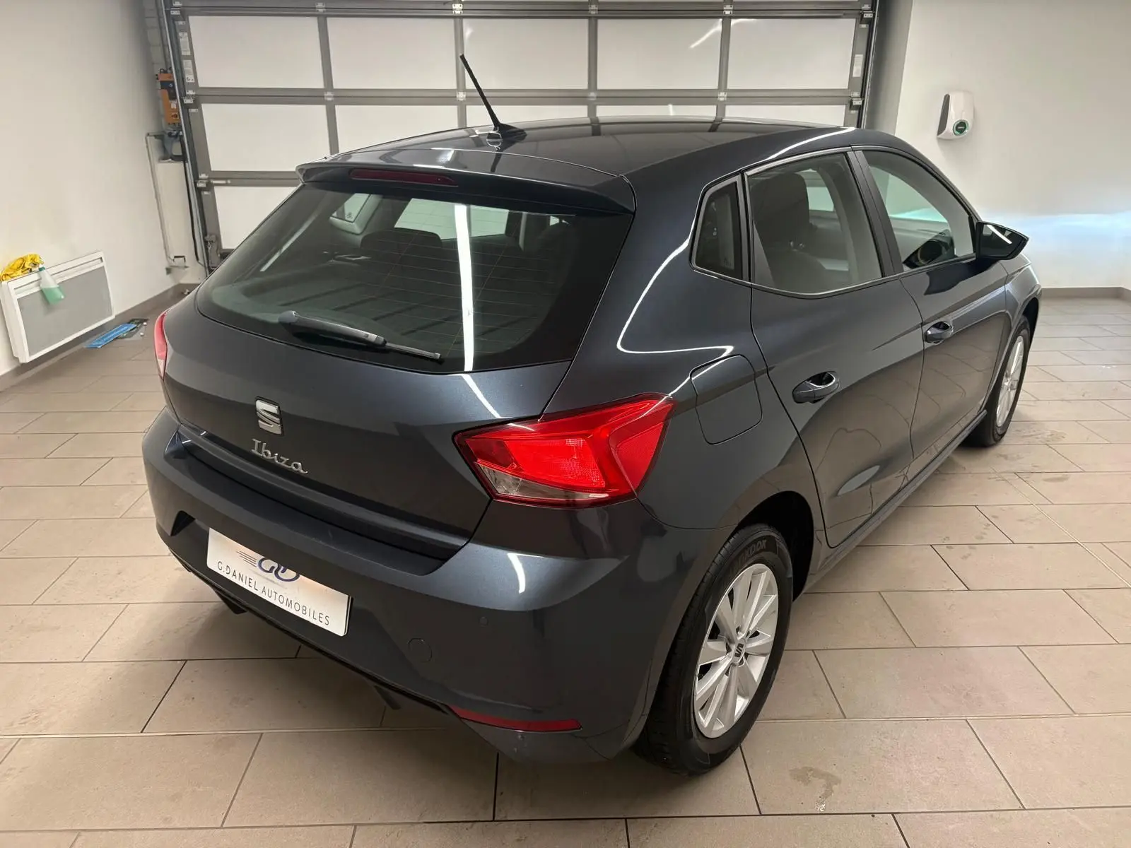 SEAT Ibiza 2024 gris magnétique vue 3/4 arrière droit dans un garage avec feux arrière rouges visibles.