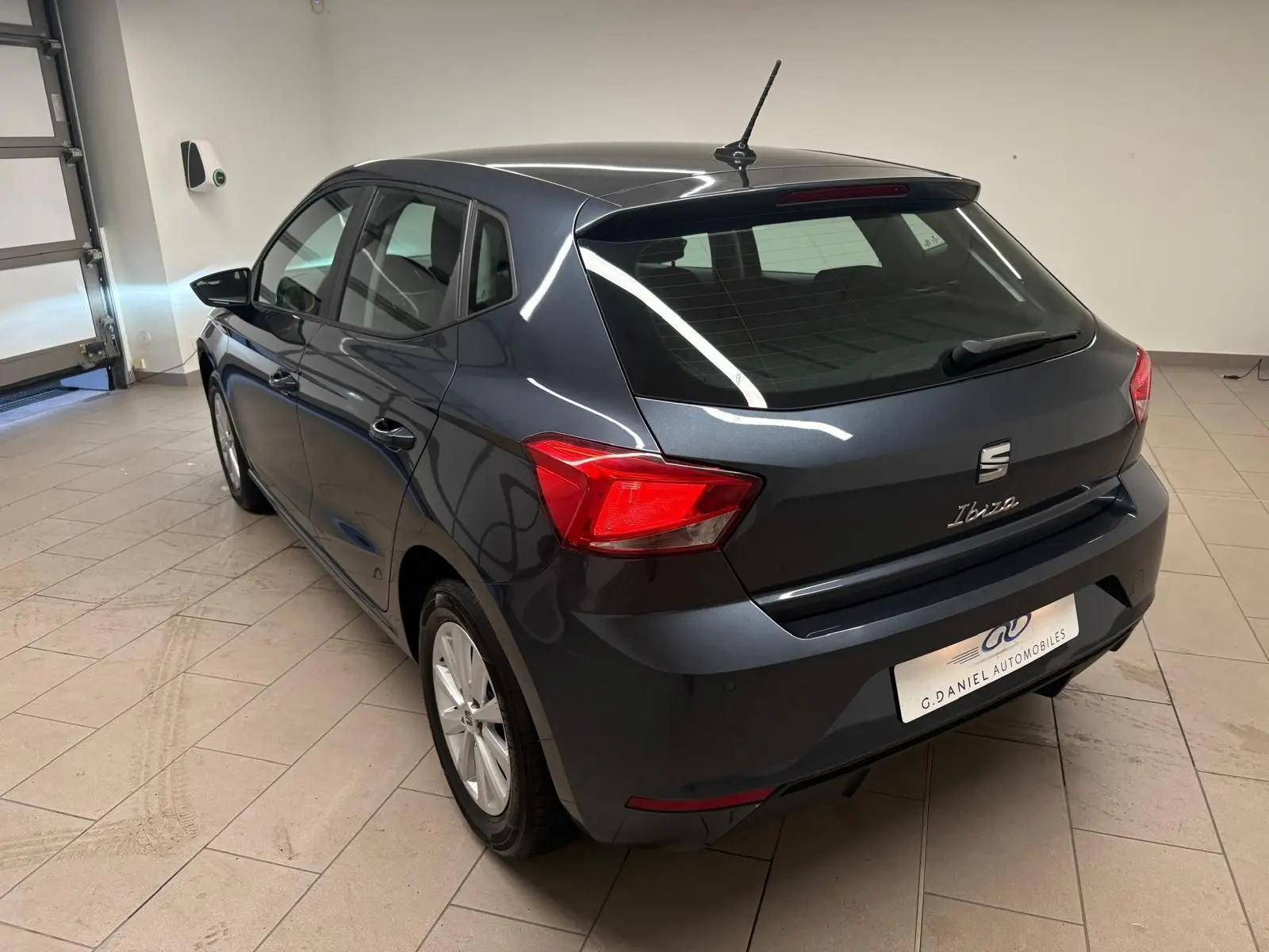 SEAT Ibiza 2024 gris magnétique vue 3/4 arrière droit en intérieur avec feux arrière rouges visibles.