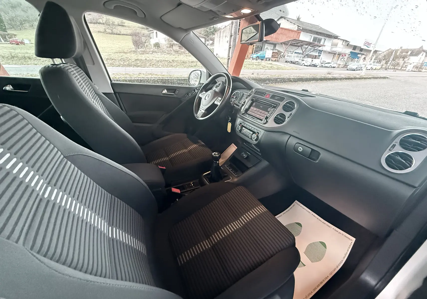 Vue intérieure côté conducteur du Volkswagen Tiguan 2.0 TDI 2010 avec sièges tissu noir et volant cuir multifonction.