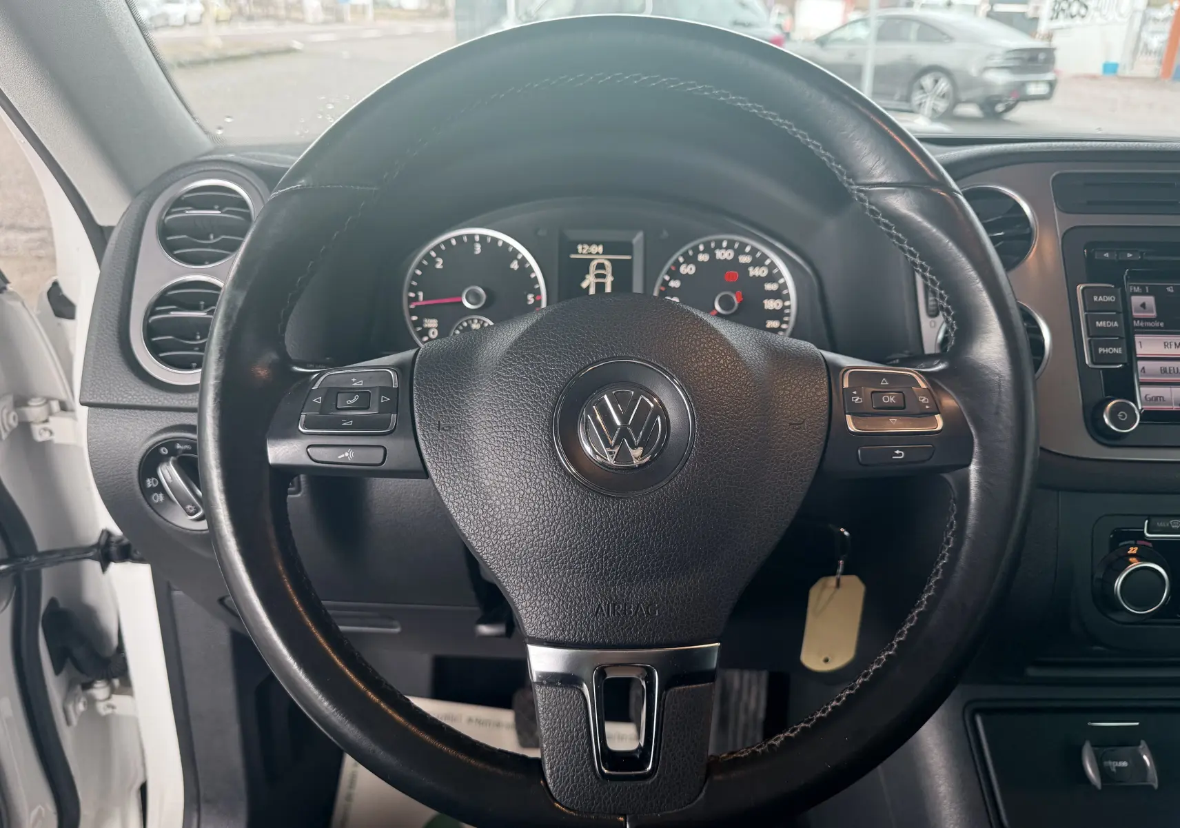 Vue intérieure centrée sur le volant en cuir noir du Volkswagen Tiguan blanc, avec tableau de bord et commandes visibles.