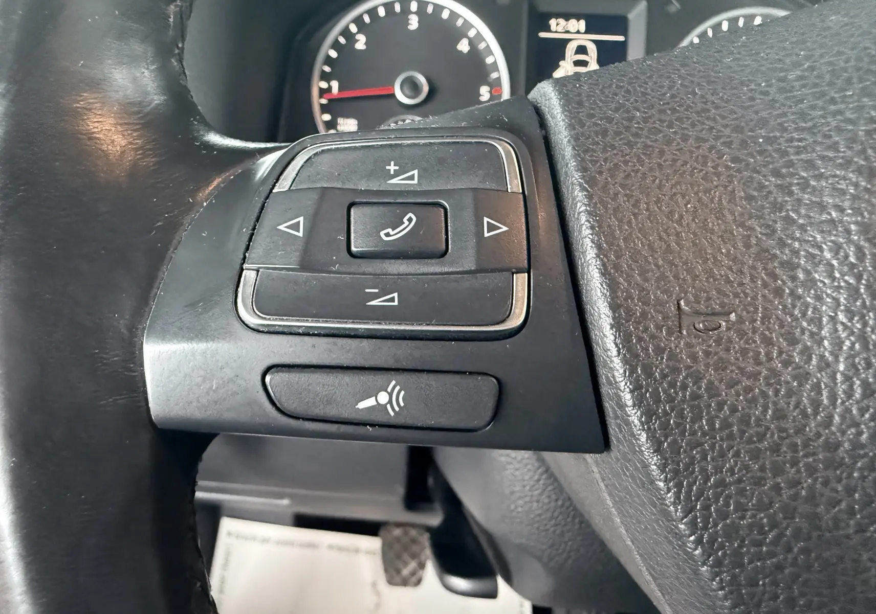 Gros plan sur les commandes au volant noir du Volkswagen Tiguan 2010, avec compteur et affichage digital en arrière-plan.