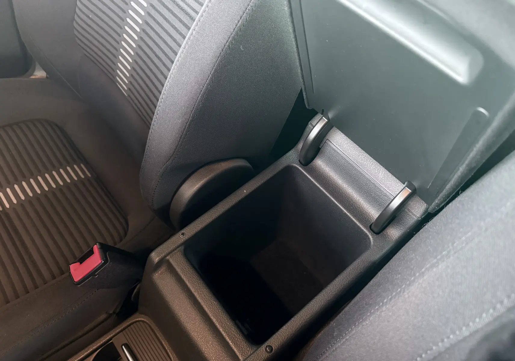 Vue intérieure rapprochée du coffre central ouvert entre les sièges avant en tissu noir du Volkswagen Tiguan blanc.