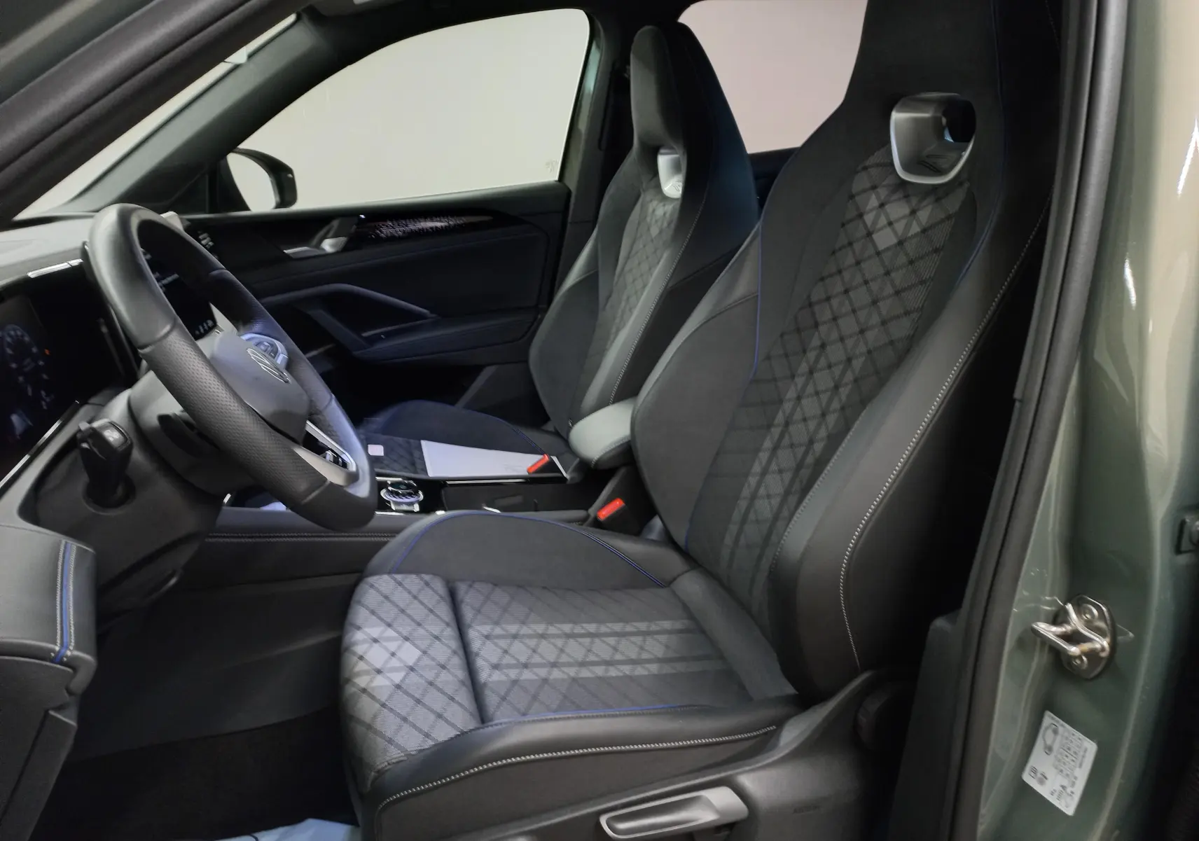 Vue intérieure côté conducteur du Volkswagen Tiguan 2025 vert Cipressino, sièges sport avec surpiqûres bleues et volant cuir.