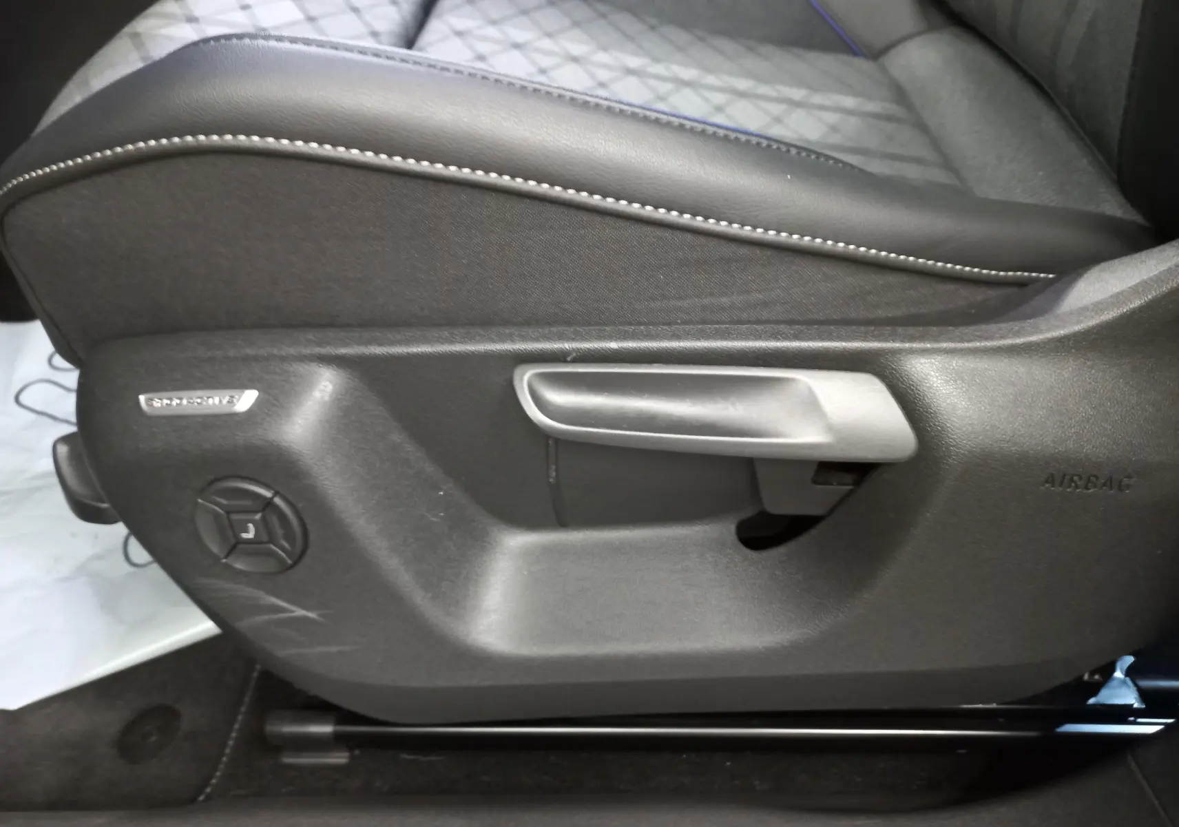 Détail du réglage manuel du siège conducteur en tissu noir avec surpiqûres blanches dans un Volkswagen Tiguan.