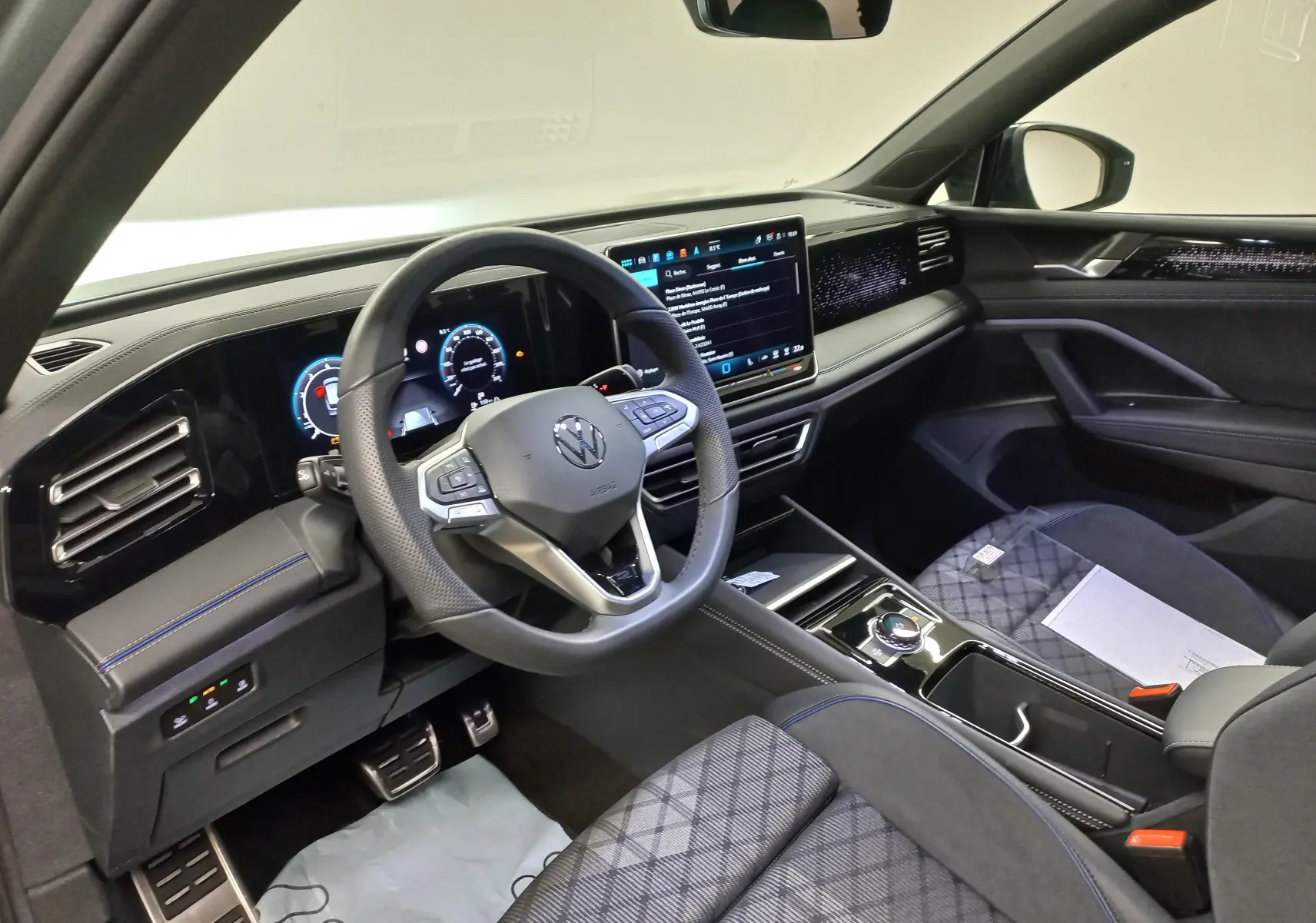 Vue intérieure côté conducteur du Volkswagen Tiguan 2025, tableau de bord numérique et sellerie tissu noir à motifs.