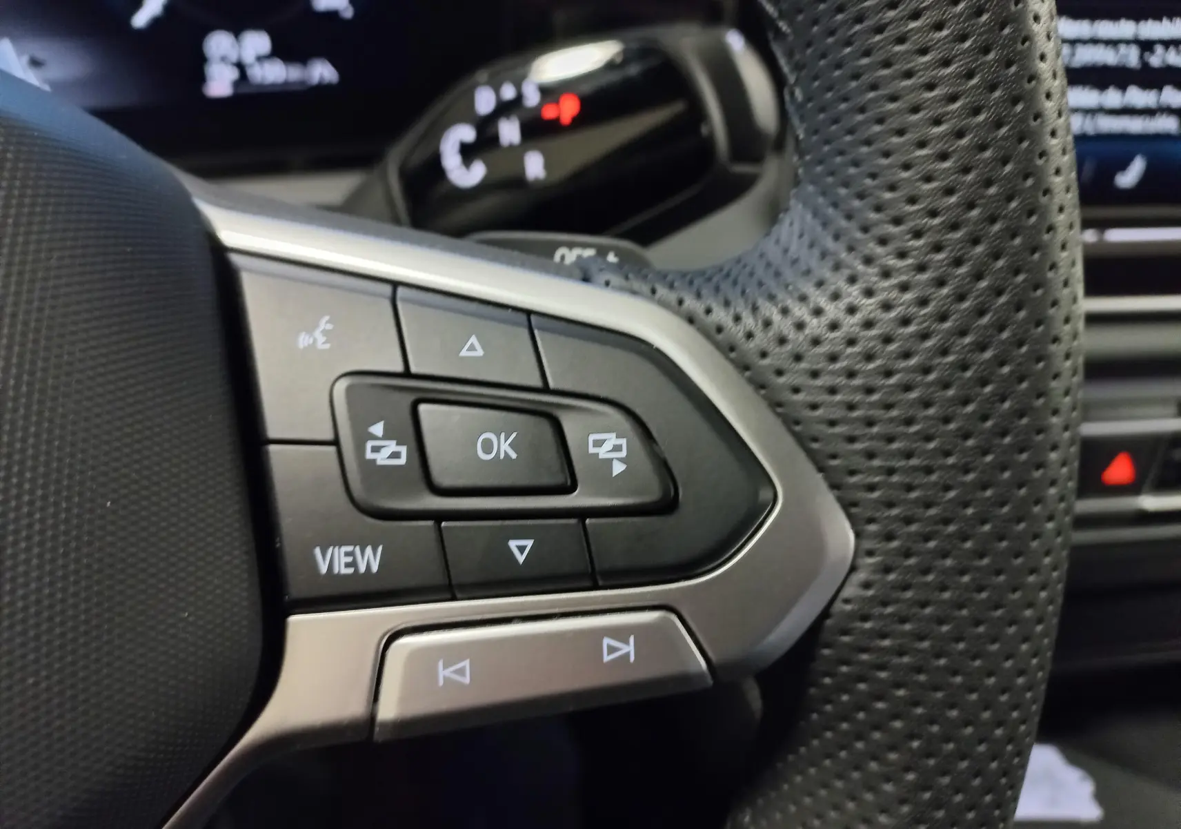 Gros plan sur les commandes multifonctions au volant perforé du Volkswagen Tiguan 2025, côté gauche, intérieur noir.