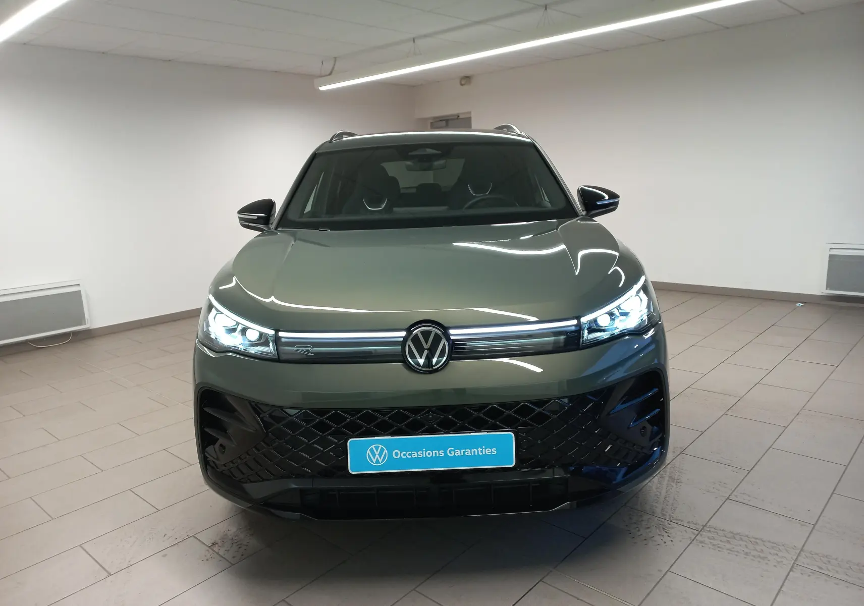 Vue frontale d'un Volkswagen Tiguan 2025 vert Cipressino avec calandre noire et phares LED allumés dans un showroom.