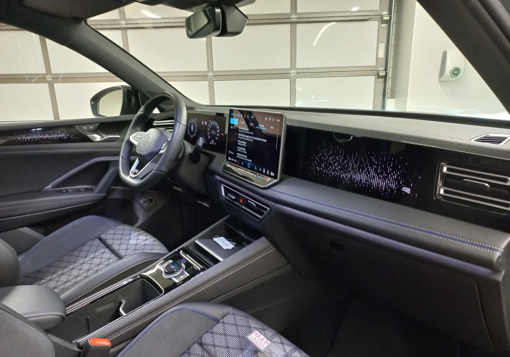 Vue intérieure côté conducteur du Volkswagen Tiguan 2025, tableau de bord numérique et sellerie tissu noire avec surpiqûres bleues.