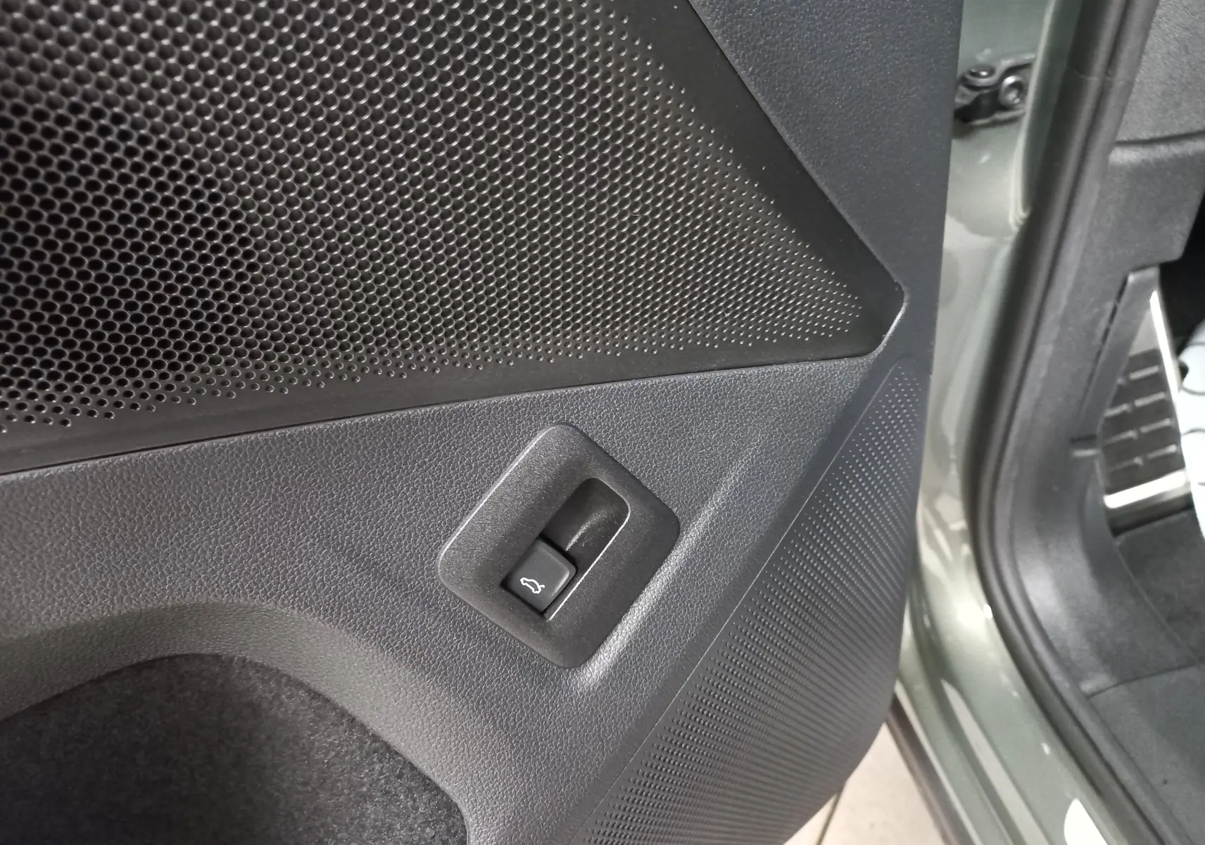 Détail du bouton d'ouverture du coffre sur la porte arrière côté gauche du Volkswagen Tiguan Vert Cipressino 2025.