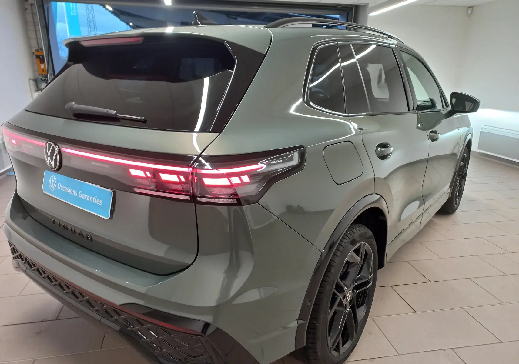 Vue 3/4 arrière droite du Volkswagen Tiguan 2025 vert Cipressino avec jantes noires et feux arrière LED allumés.