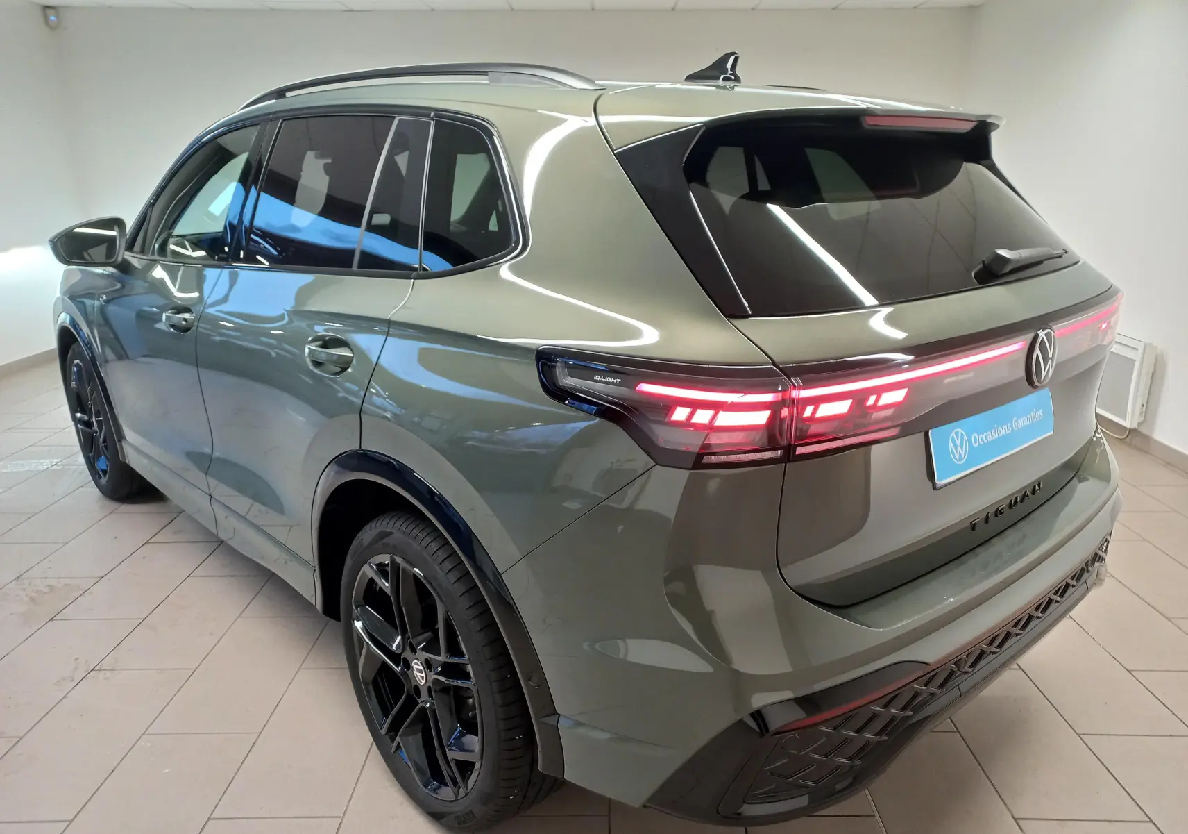 Vue 3/4 arrière droite du Volkswagen Tiguan 2025 vert Cipressino avec jantes noires et feux LED allumés.