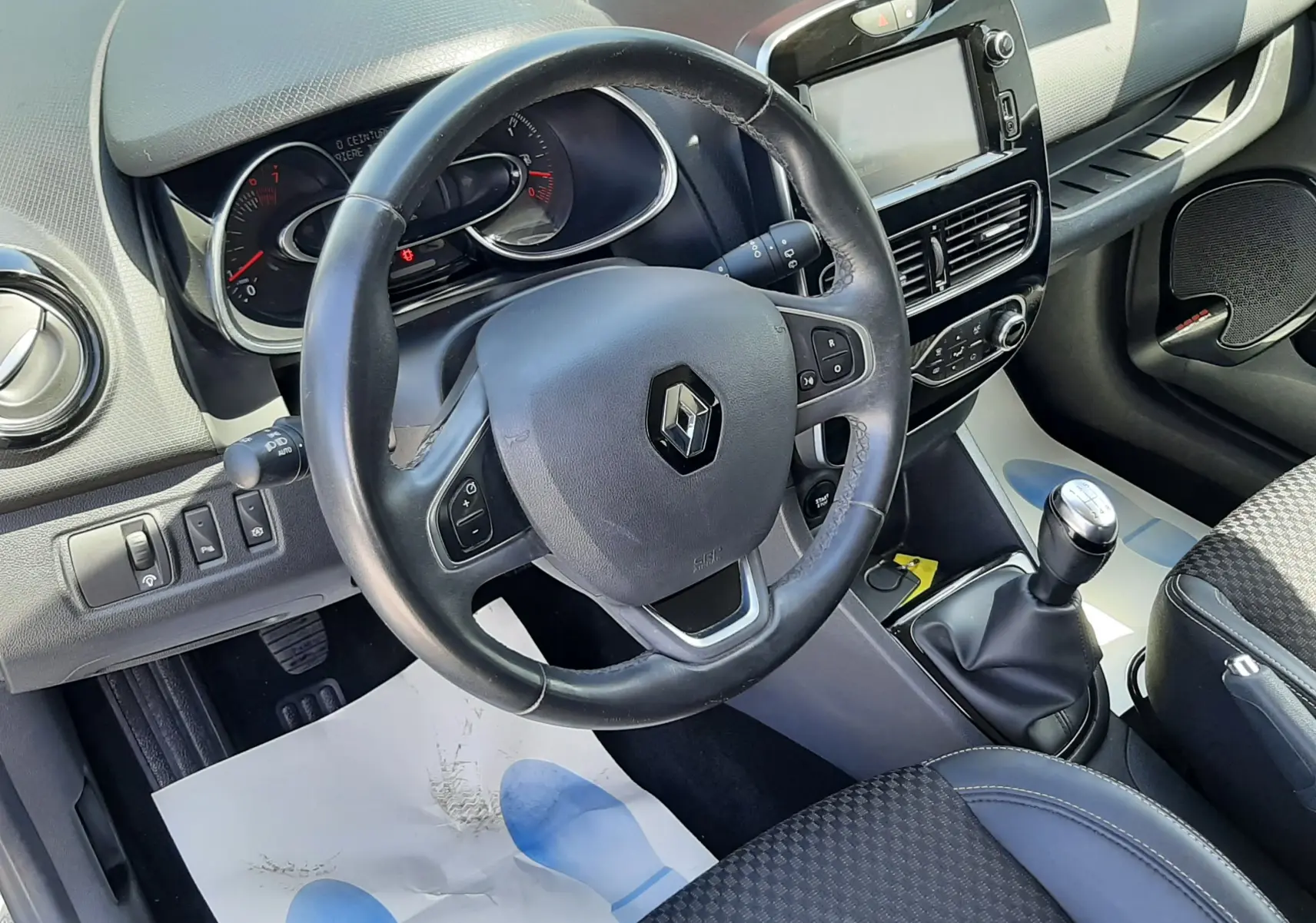 Vue intérieure de face du poste de conduite de la Renault Clio IV gris titanium, volant multifonction et levier de vitesses manuel visibles.