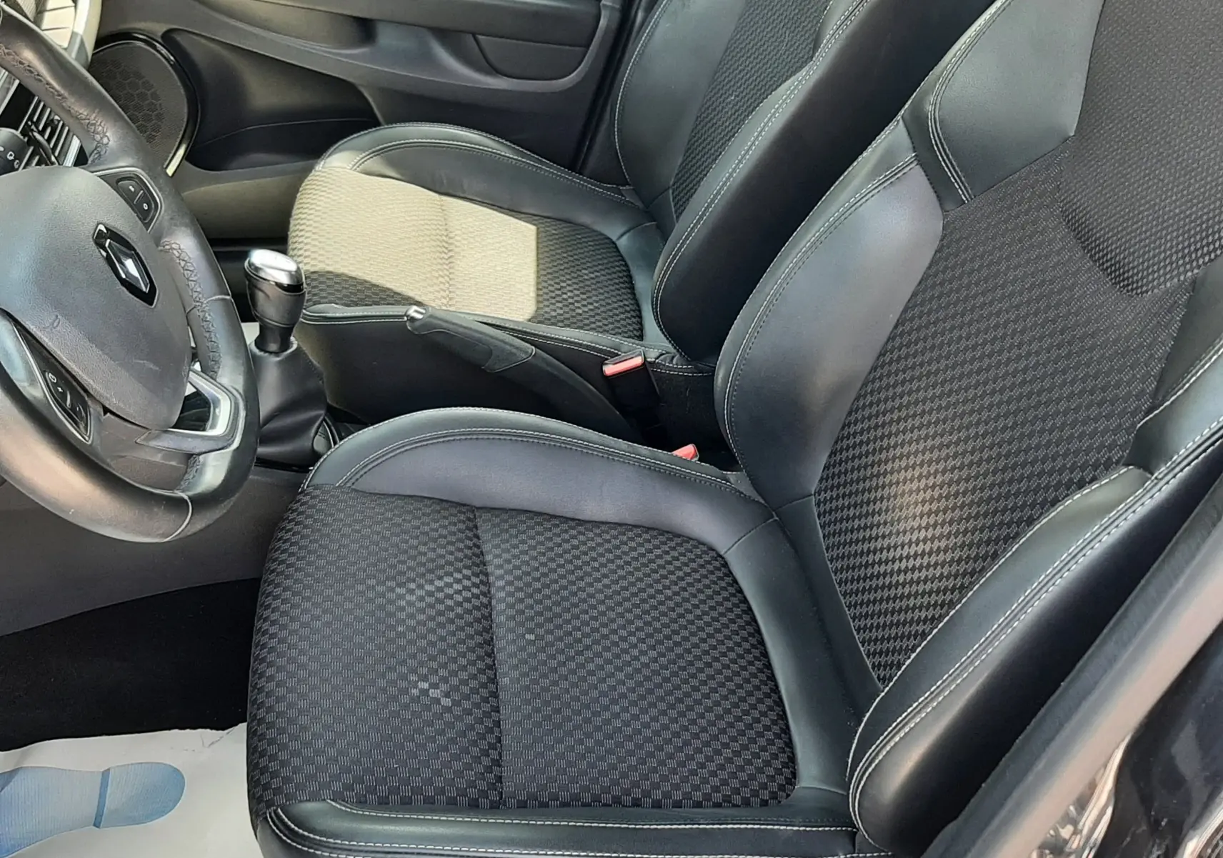 Vue intérieure côté conducteur de la Renault Clio IV gris titanium, sièges noirs en tissu et cuir avec volant multifonction.