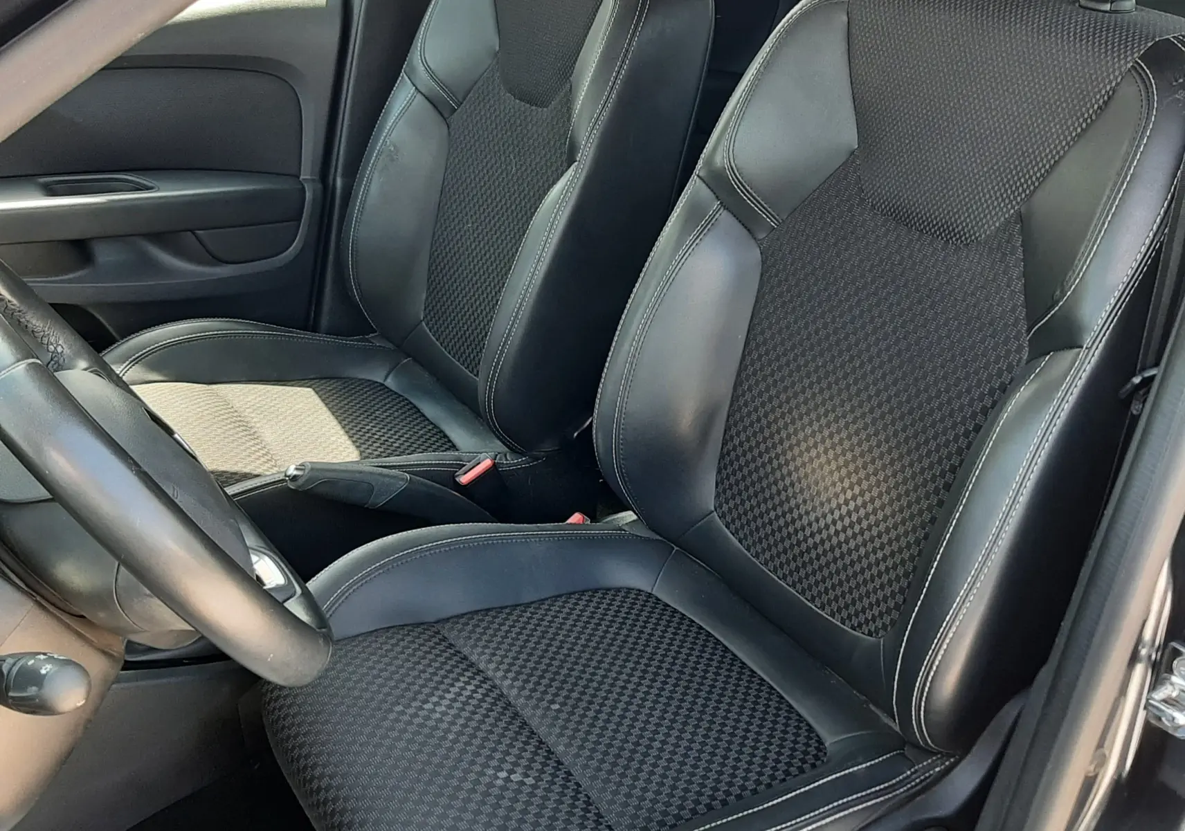 Vue intérieure côté conducteur de la Renault Clio IV 0.9 TCE 90 Intens, sièges noirs en cuir et tissu avec surpiqûres blanches.