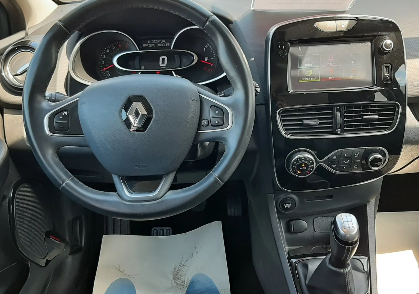 Vue intérieure frontale du tableau de bord et volant noir de la Renault Clio IV gris titanium, avec levier de vitesses manuel et écran tactile.