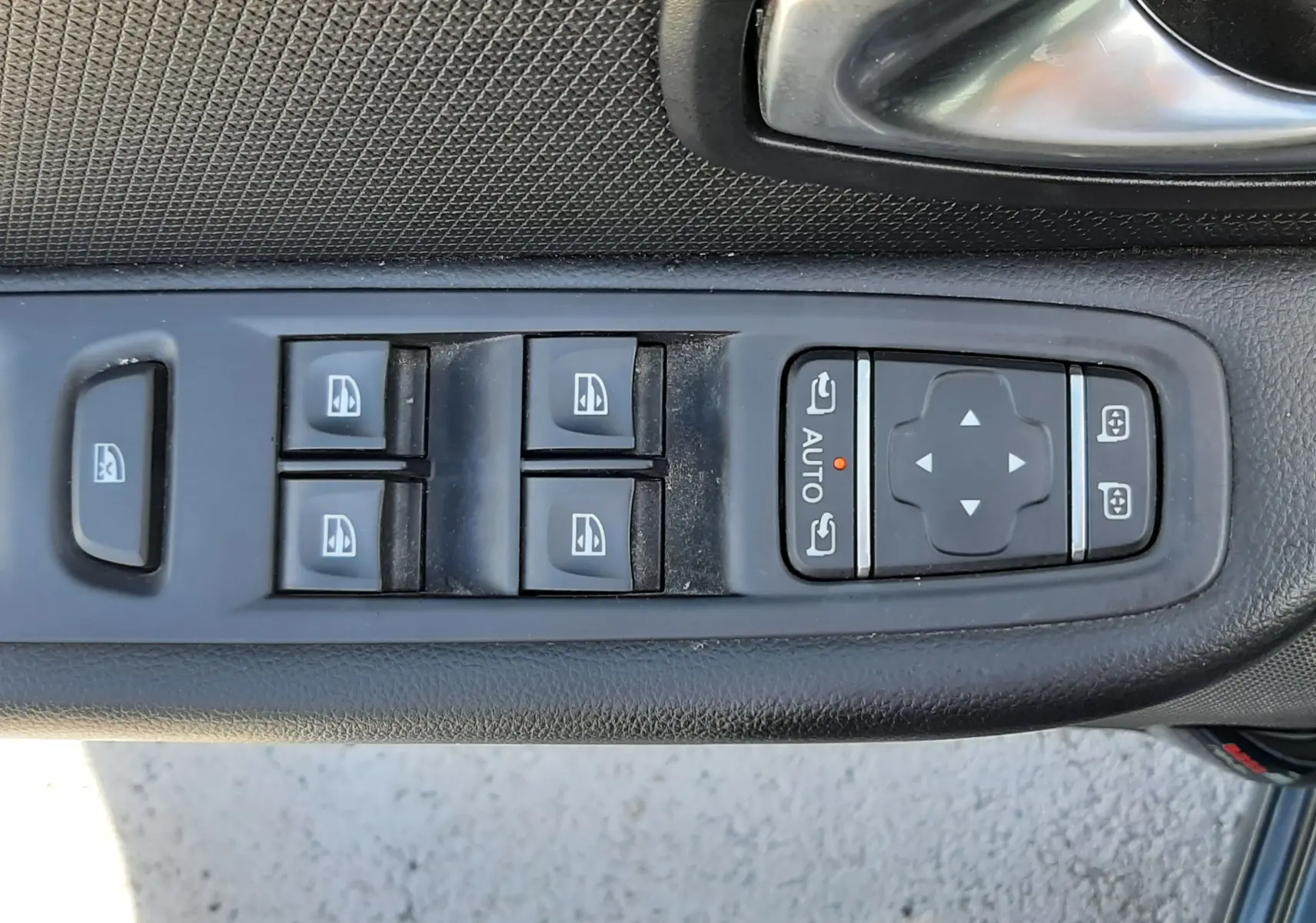 Gros plan sur la commande des vitres électriques et réglages des rétroviseurs côté conducteur d'une Renault Clio IV gris titanium.