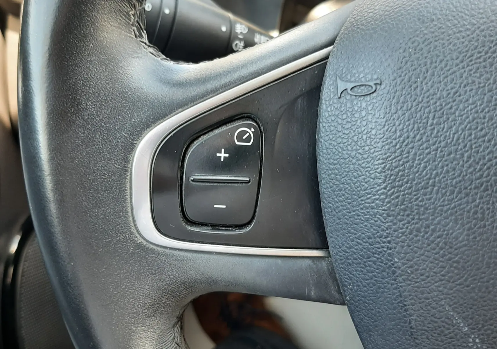 Gros plan sur les commandes de régulateur de vitesse à gauche du volant noir de la Renault Clio IV gris titanium.