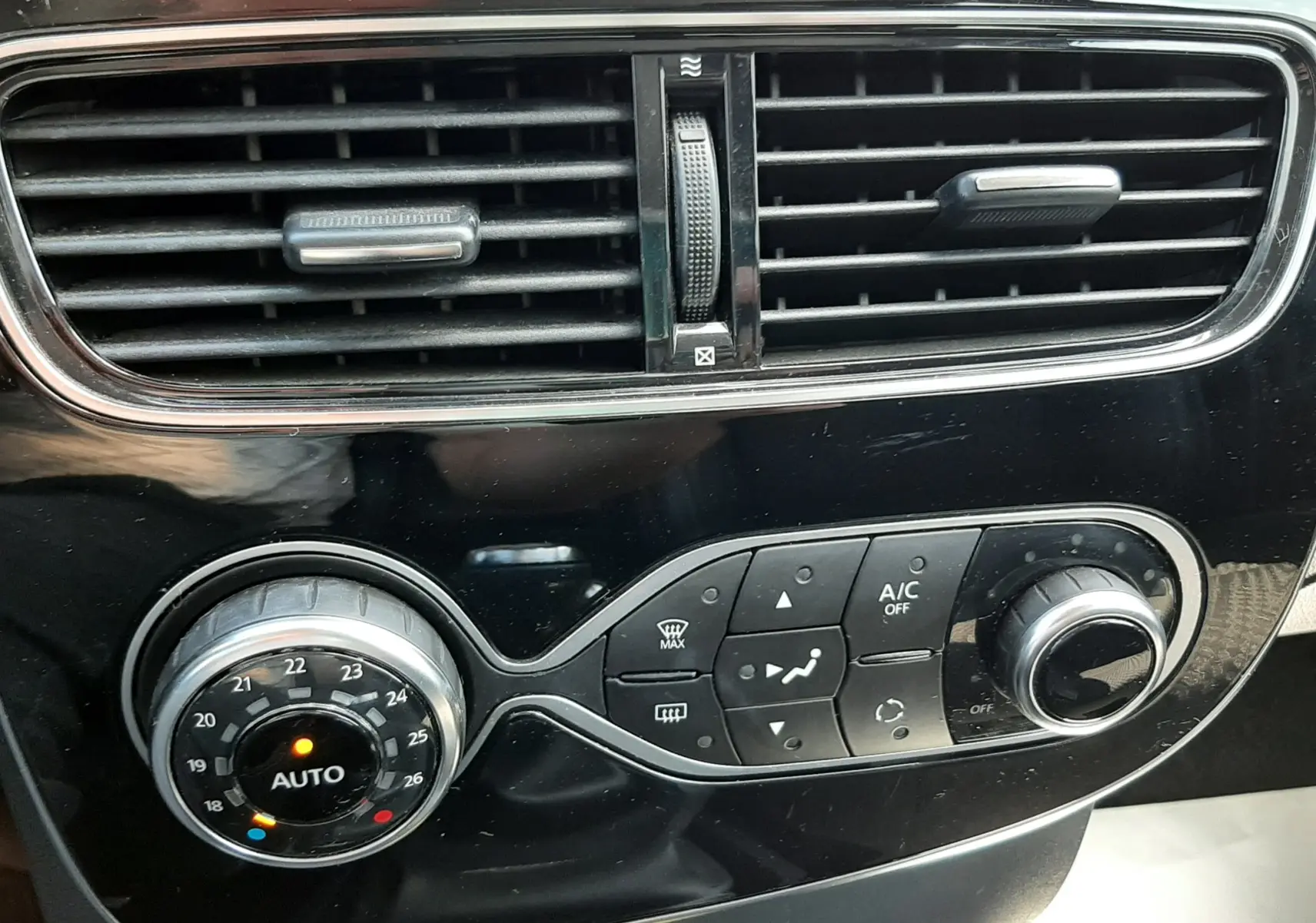 Gros plan sur la console centrale noire de la Renault Clio IV, montrant les commandes de climatisation et les aérateurs horizontaux.