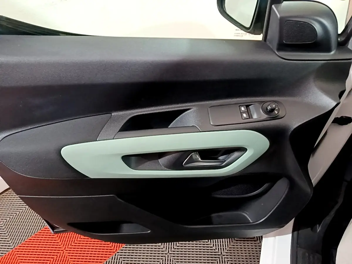 Vue intérieure côté gauche de la porte avant d'un Citroën Berlingo blanc, avec poignée vert clair et commandes électriques.