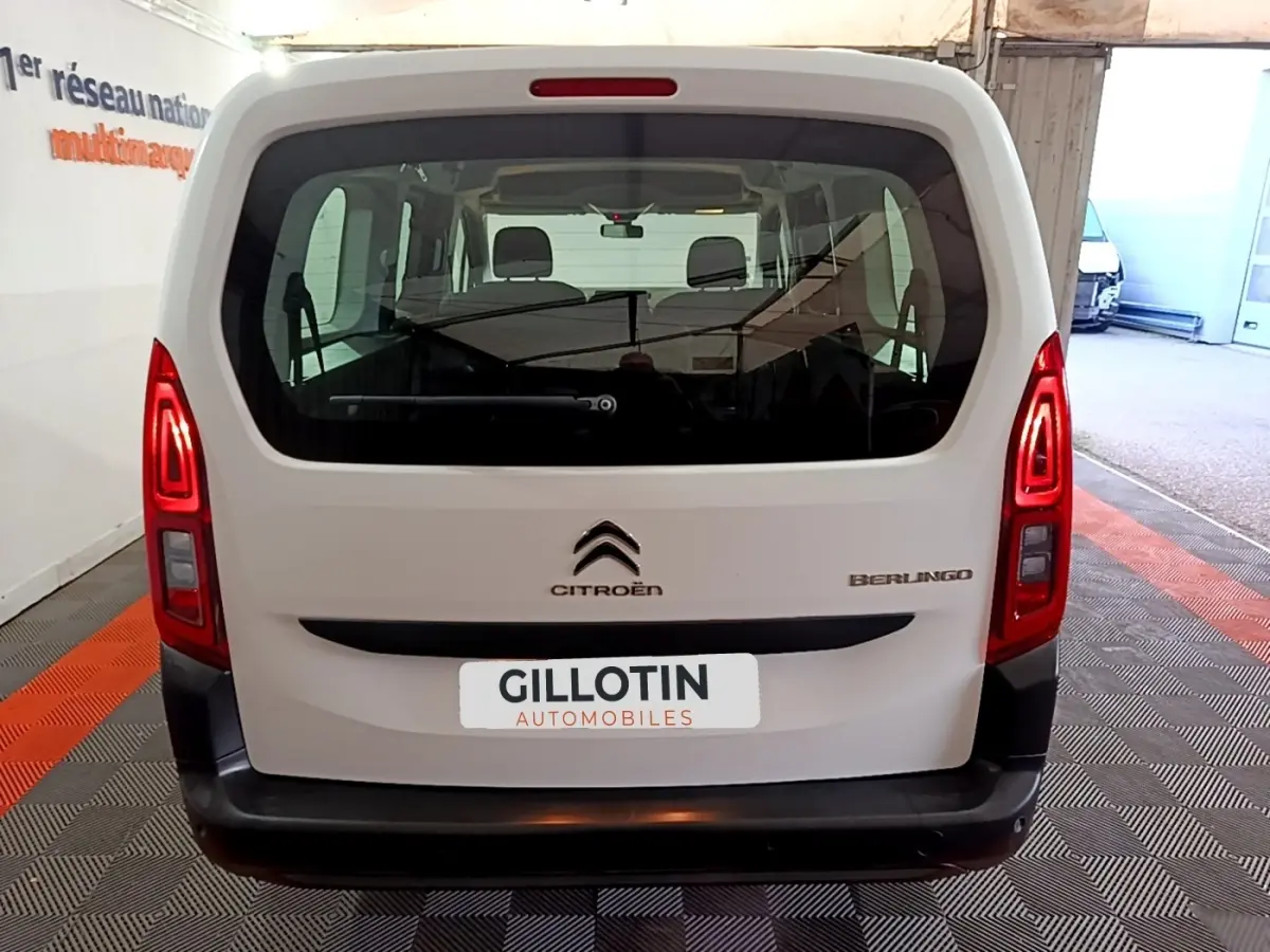 Vue arrière d'un Citroën Berlingo blanc XL, avec feux arrière allumés et vitre arrière large visible en intérieur.
