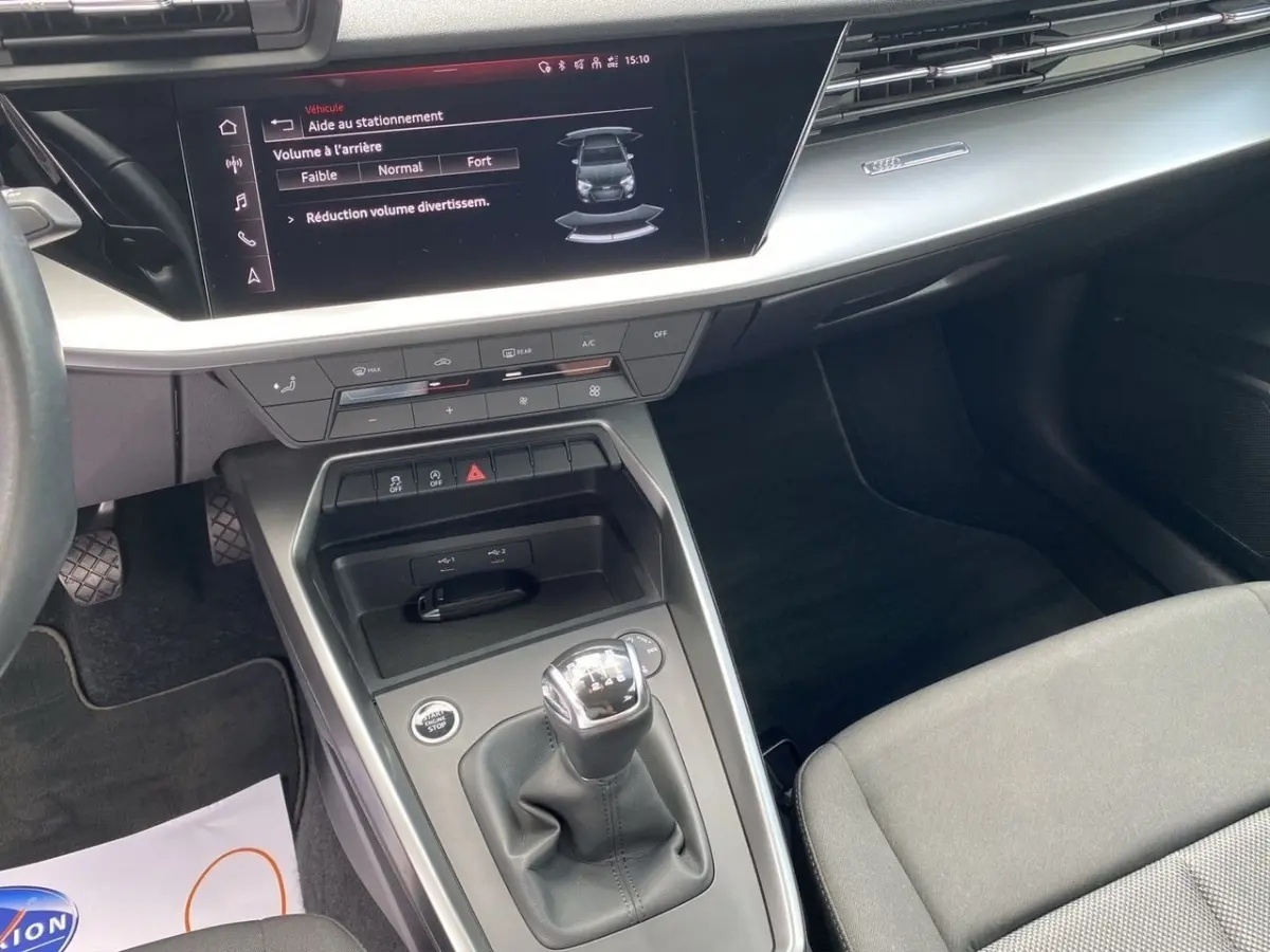Vue intérieure centrée sur la console centrale d'une Audi A3 gris foncé, avec levier de vitesses manuel et écran tactile.