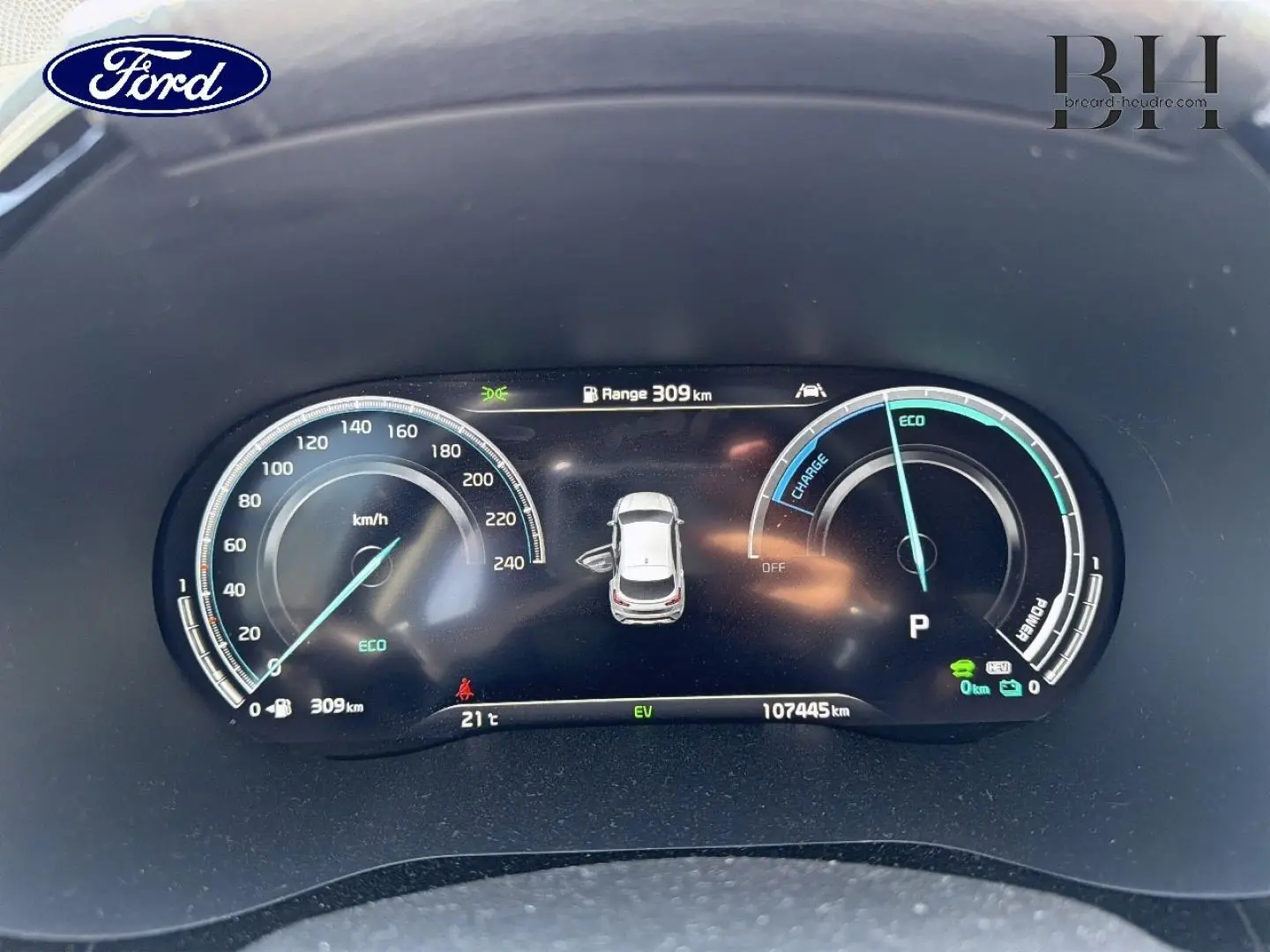 Image d'un tableau de bord numérique d'une Kia Xceed noire, affichant la vitesse, l'autonomie et l'état hybride rechargeable.