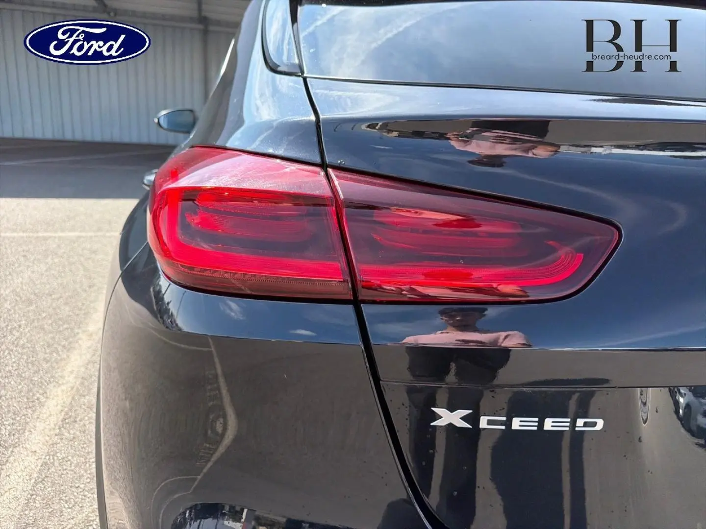 Gros plan sur le feu arrière gauche d'un KIA Xceed noir Basalte métallisé, avec logo et reflet sur la carrosserie.