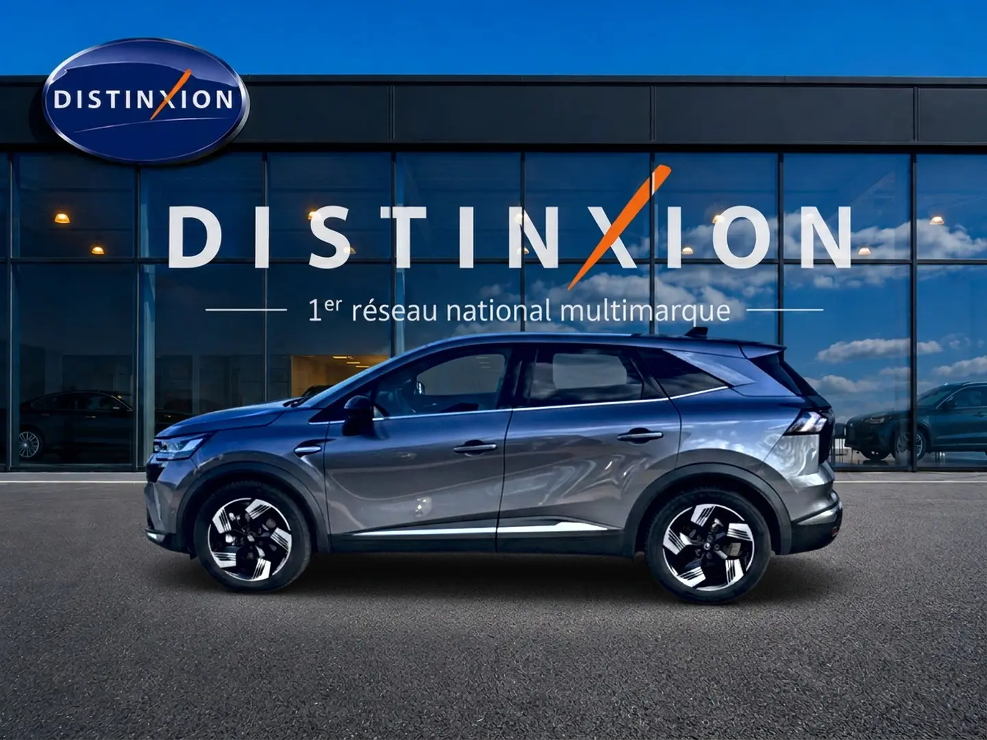 Renault Symbioz gris en profil droit devant une vitrine Distinxion, avec jantes noires et toit surélevé.