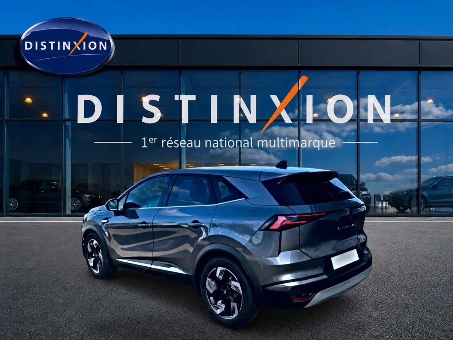 Renault Symbioz gris en 3/4 arrière droit, avec jantes noires et toit noir devant une vitrine Distinxion.