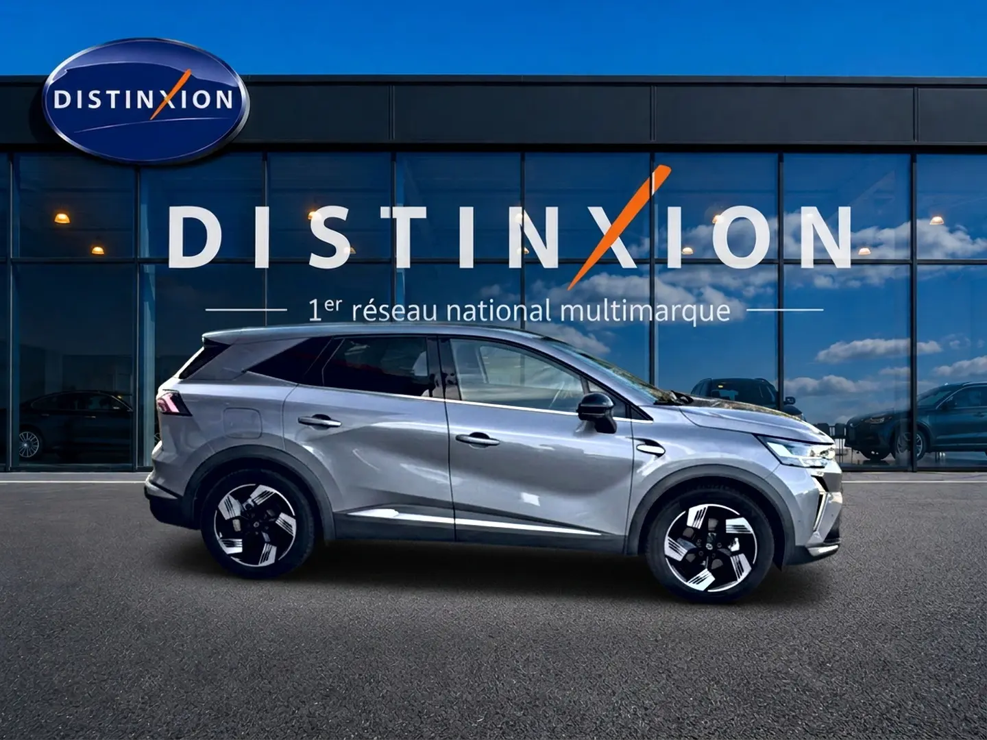 Profil droit de la Renault Symbioz gris 2025, SUV hybride avec jantes noires et toit surélevé devant vitrine Distinxion.