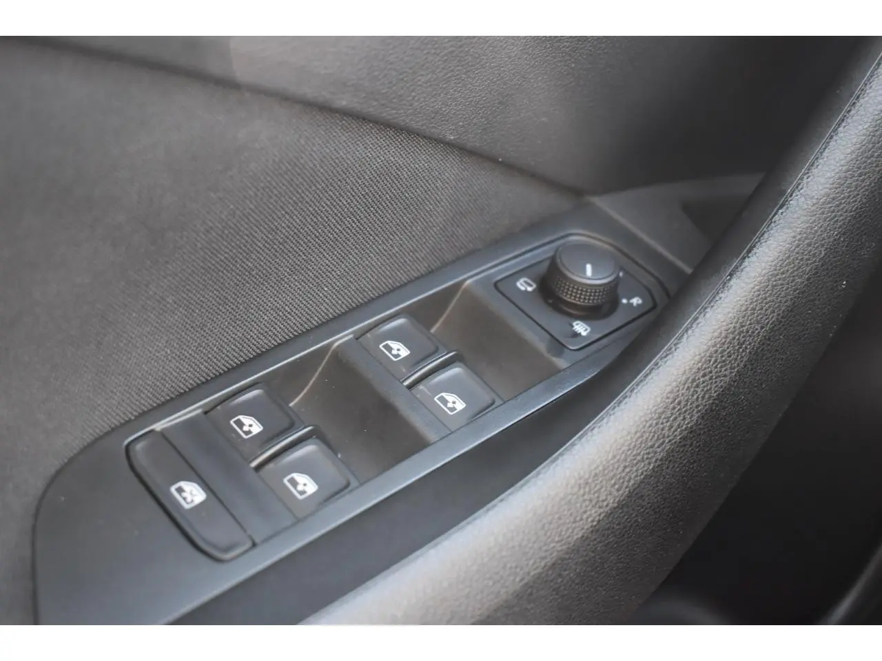 Gros plan sur les commandes de lève-vitres et réglage des rétroviseurs côté conducteur d'une Skoda Scala blanche.