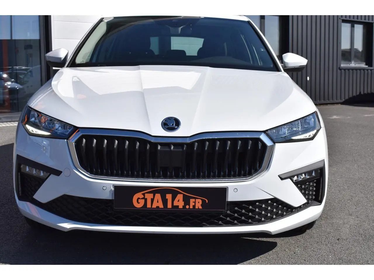 Vue frontale d'une Skoda Scala blanche Glacier avec calandre noire et phares LED anguleux sur parking.