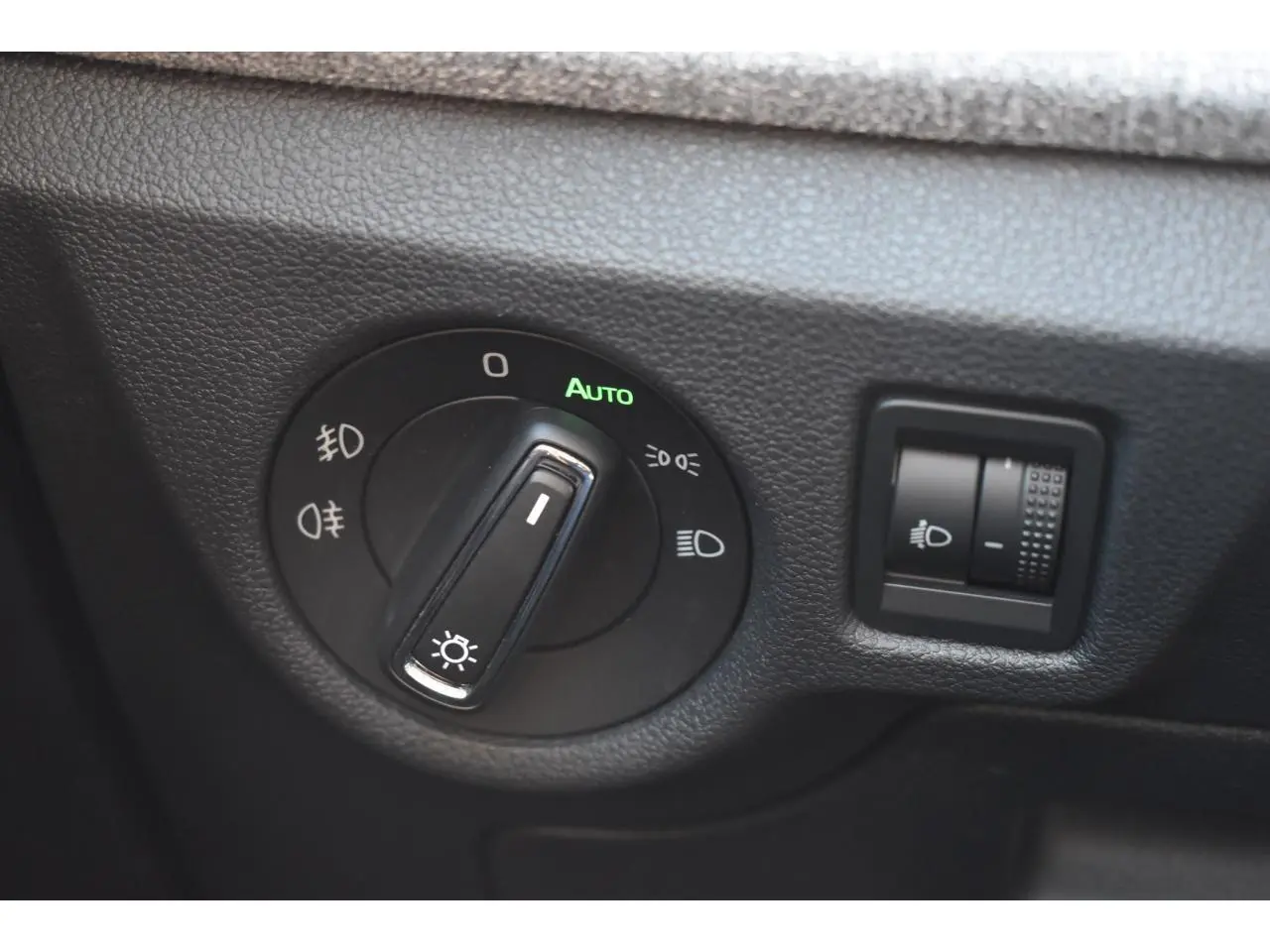 Gros plan sur le bouton de commande des phares avec réglage automatique dans l'habitacle noir d'une Skoda Scala.