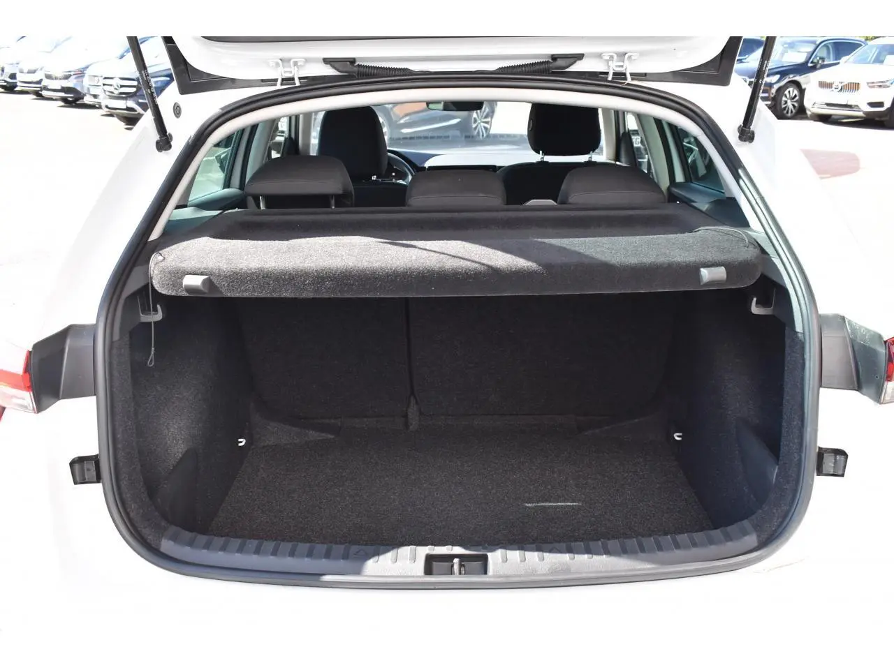Coffre ouvert vu de l'arrière d'une Skoda Scala blanc glacier, avec cache-bagages et banquette arrière noire visible.