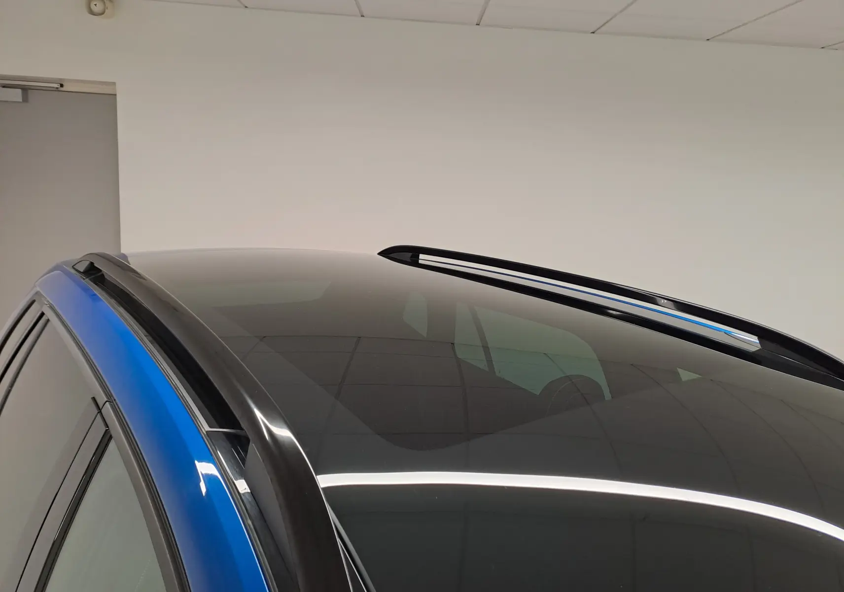 Toit panoramique noir brillant et barres de toit noires sur un Skoda Kamiq Bleu RS, vue en léger contre-plongée côté gauche.