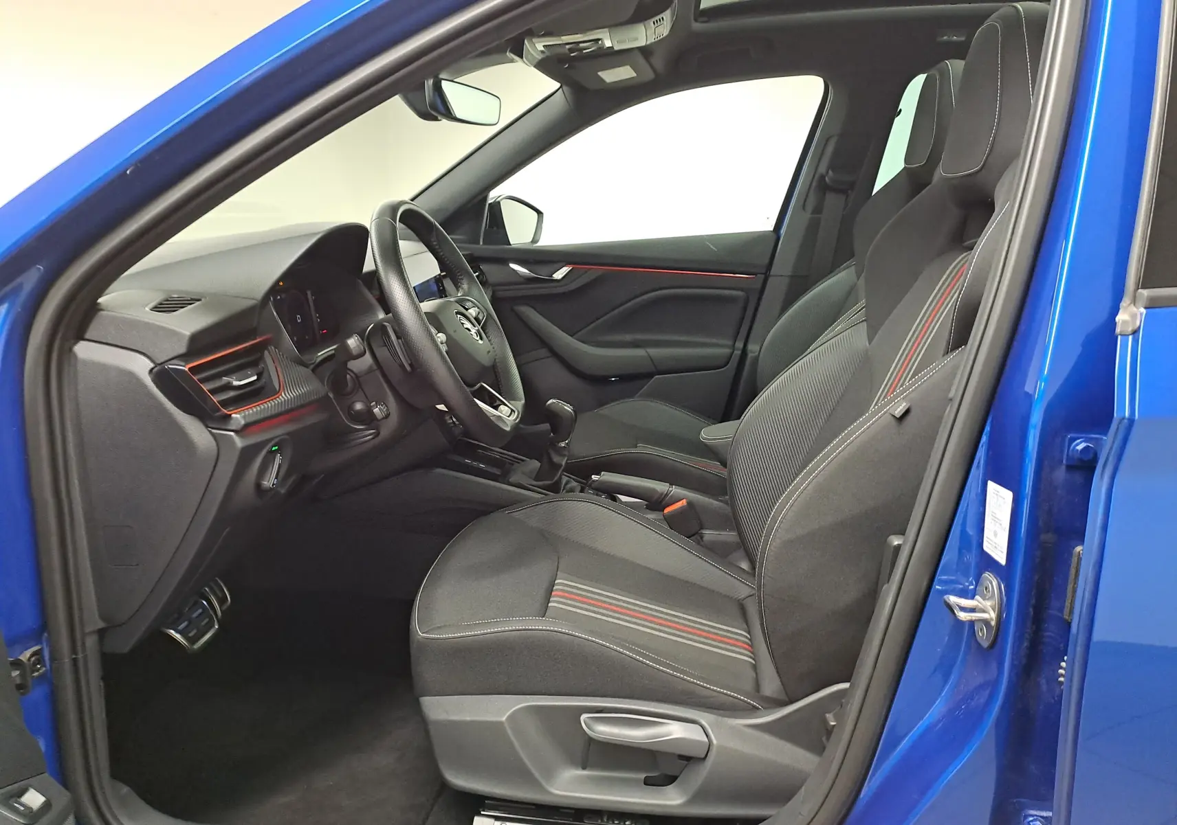 Intérieur côté conducteur du Skoda Kamiq Bleu RS 2024, sièges sport avec surpiqûres rouges et tableau de bord moderne.