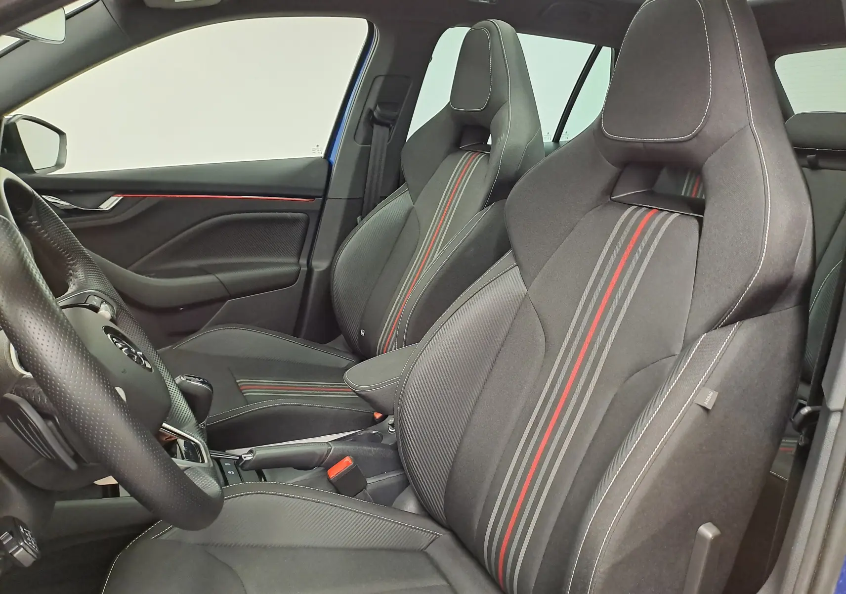 Vue intérieure côté conducteur du Skoda Kamiq 2024 bleu RS, sièges sport noirs avec bandes grises et rouges.