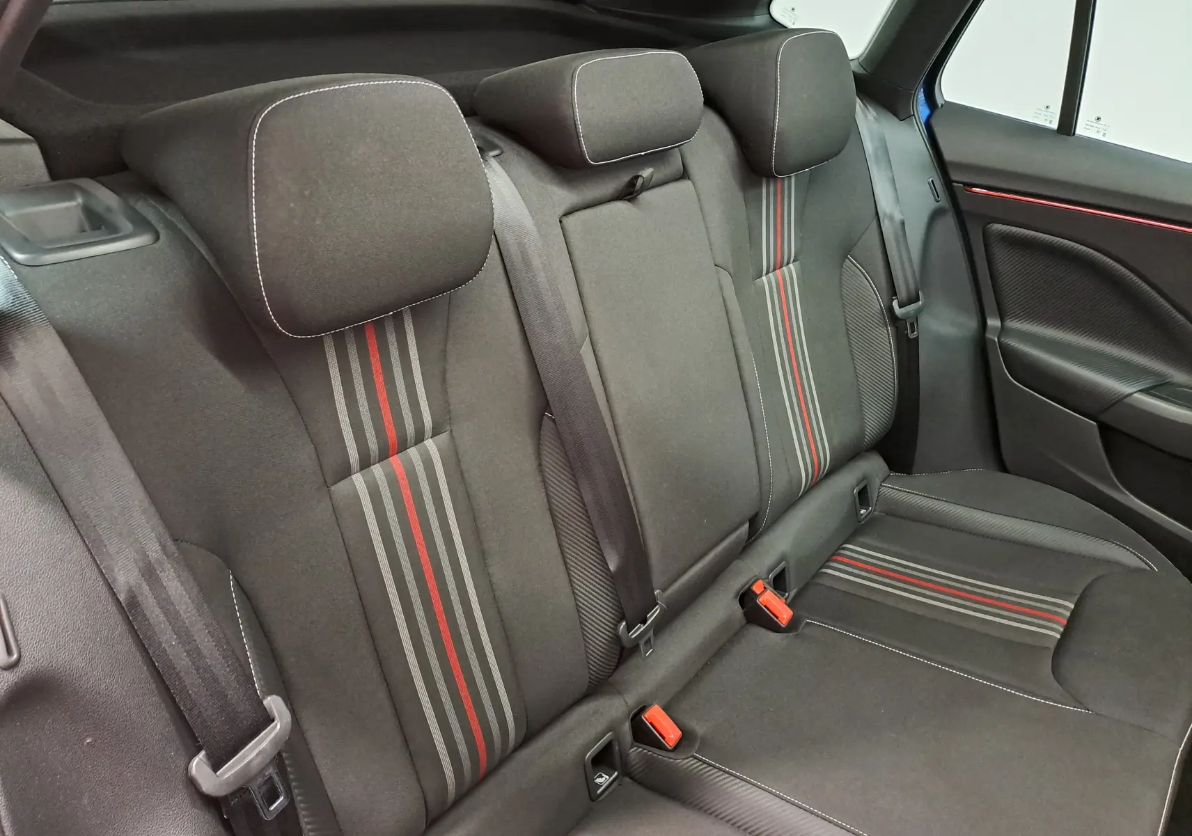 Vue intérieure des sièges arrière du Skoda Kamiq Monte Carlo 2024, tissu noir avec bandes grises et rouges, ceinture de sécurité visible.