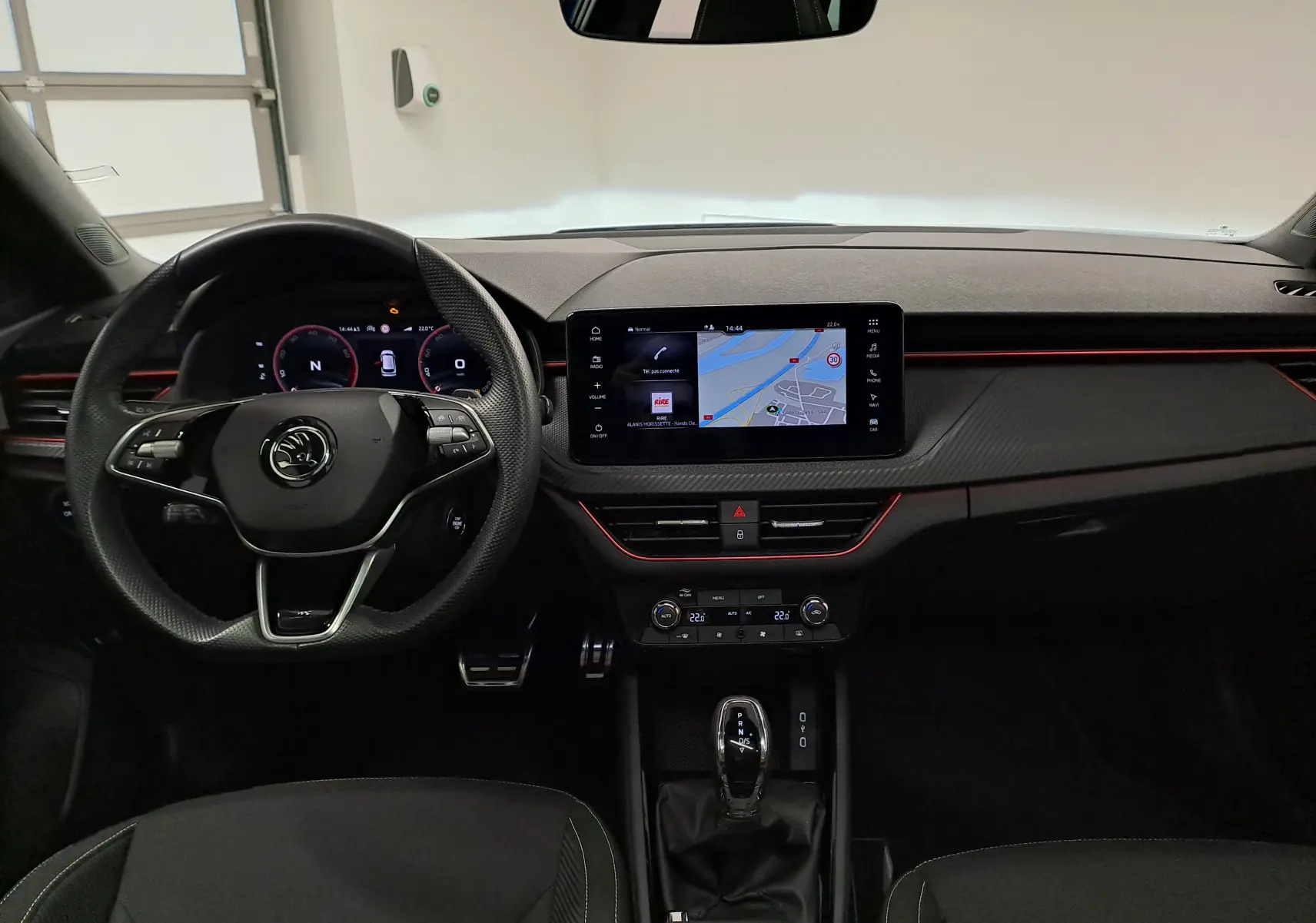 Vue intérieure frontale du Skoda Kamiq 2024, tableau de bord noir avec éclairage rouge et écran tactile central affichant la navigation.