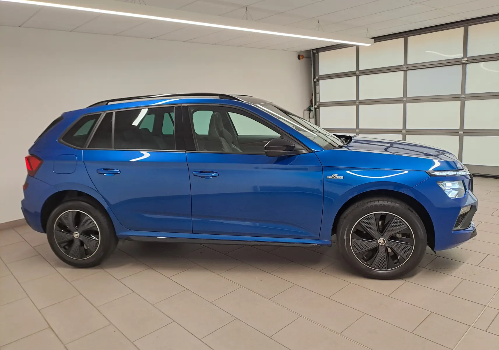 Vue de profil côté gauche du Skoda Kamiq 1.5 TSI 150 DSG7 Monte Carlo en bleu RS avec jantes noires distinctives.