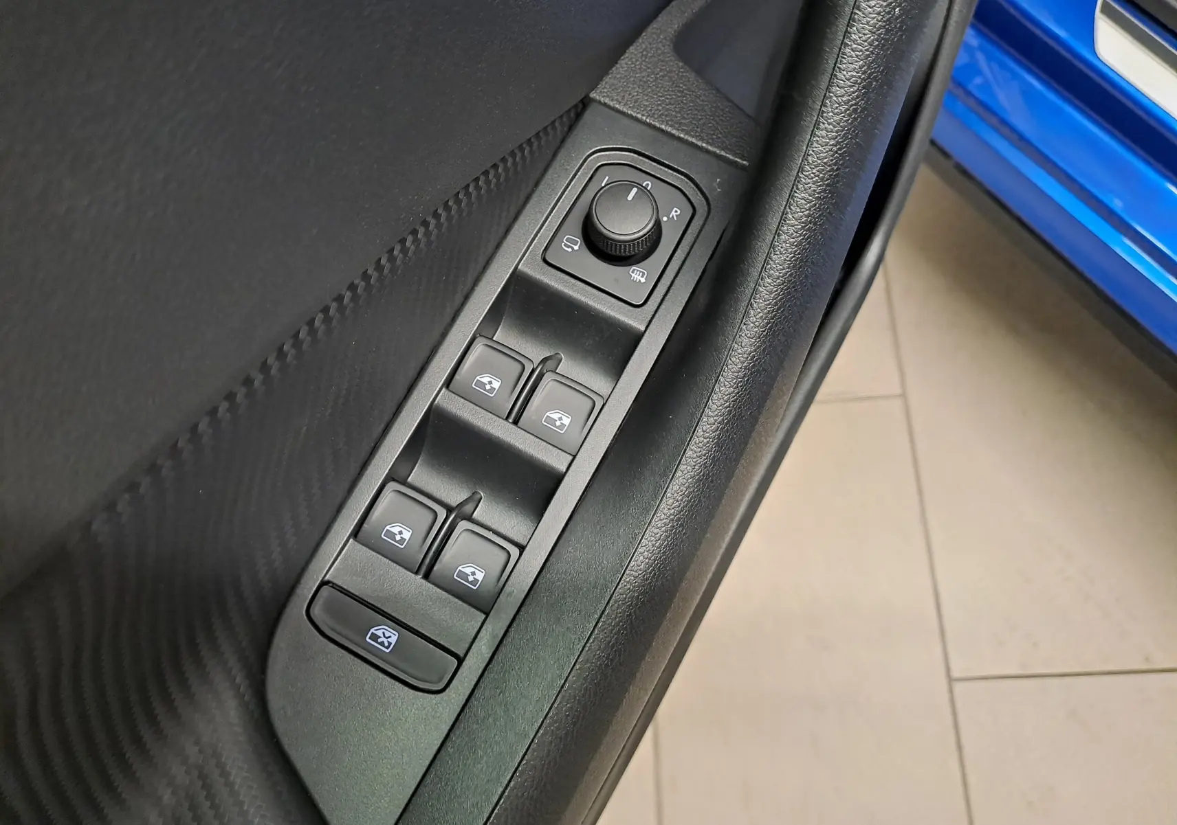 Gros plan sur les commandes de lève-vitres et rétroviseurs côté conducteur d'une Skoda Kamiq bleu RS visible à l'arrière.