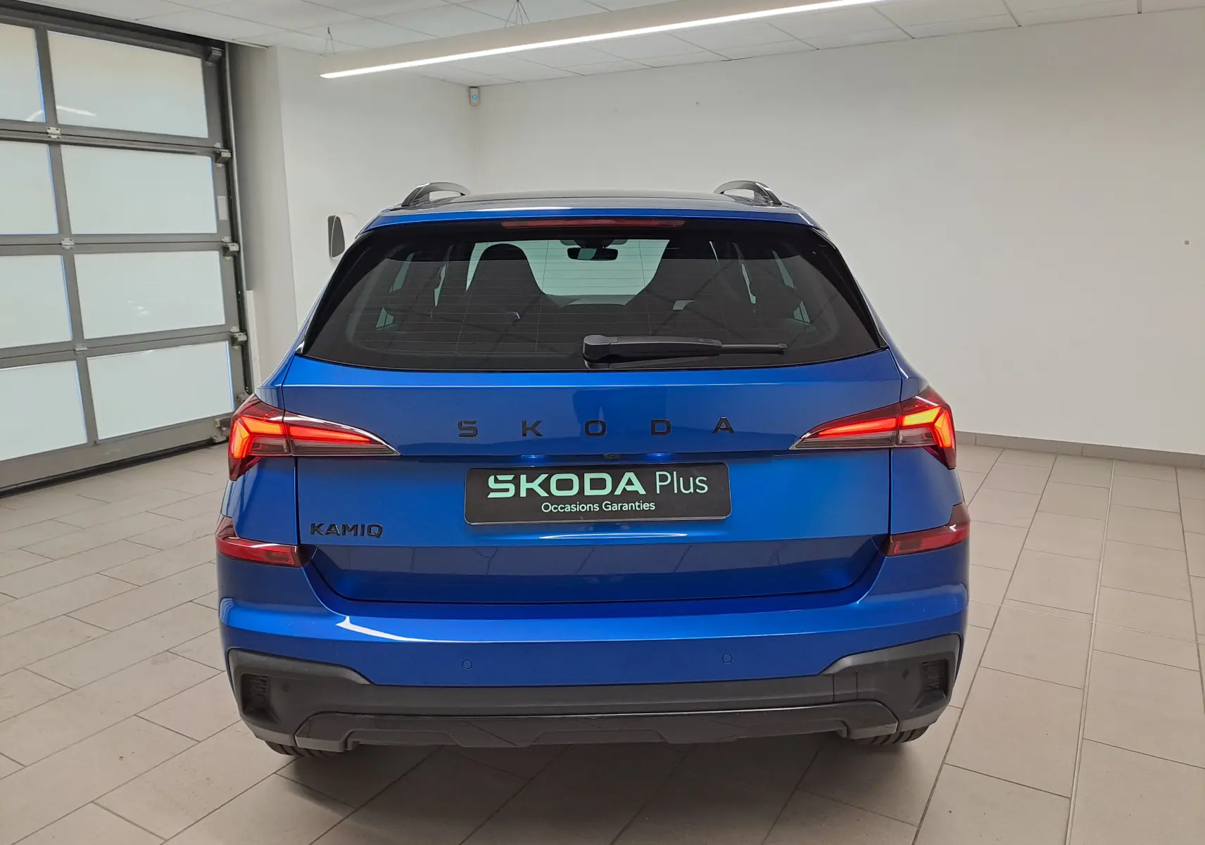 Vue arrière d'un Skoda Kamiq Bleu RS 2024 en intérieur, avec feux arrière allumés et hayon fermé.