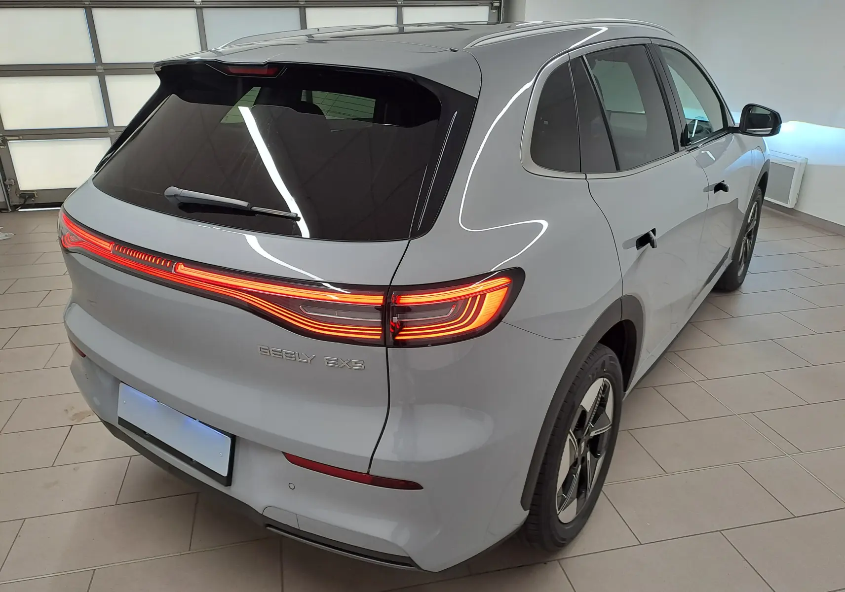 Vue 3/4 arrière droite du SUV électrique Geely E5 PRO gris Moonlight avec feux arrière allumés en intérieur.