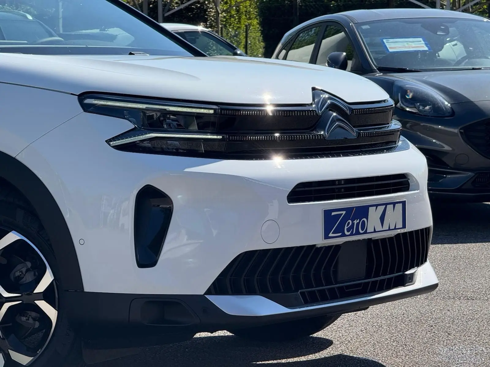 Vue 3/4 avant droite du Citroën C5 Aircross blanc banquise avec calandre noire et plaque Zero KM visible.