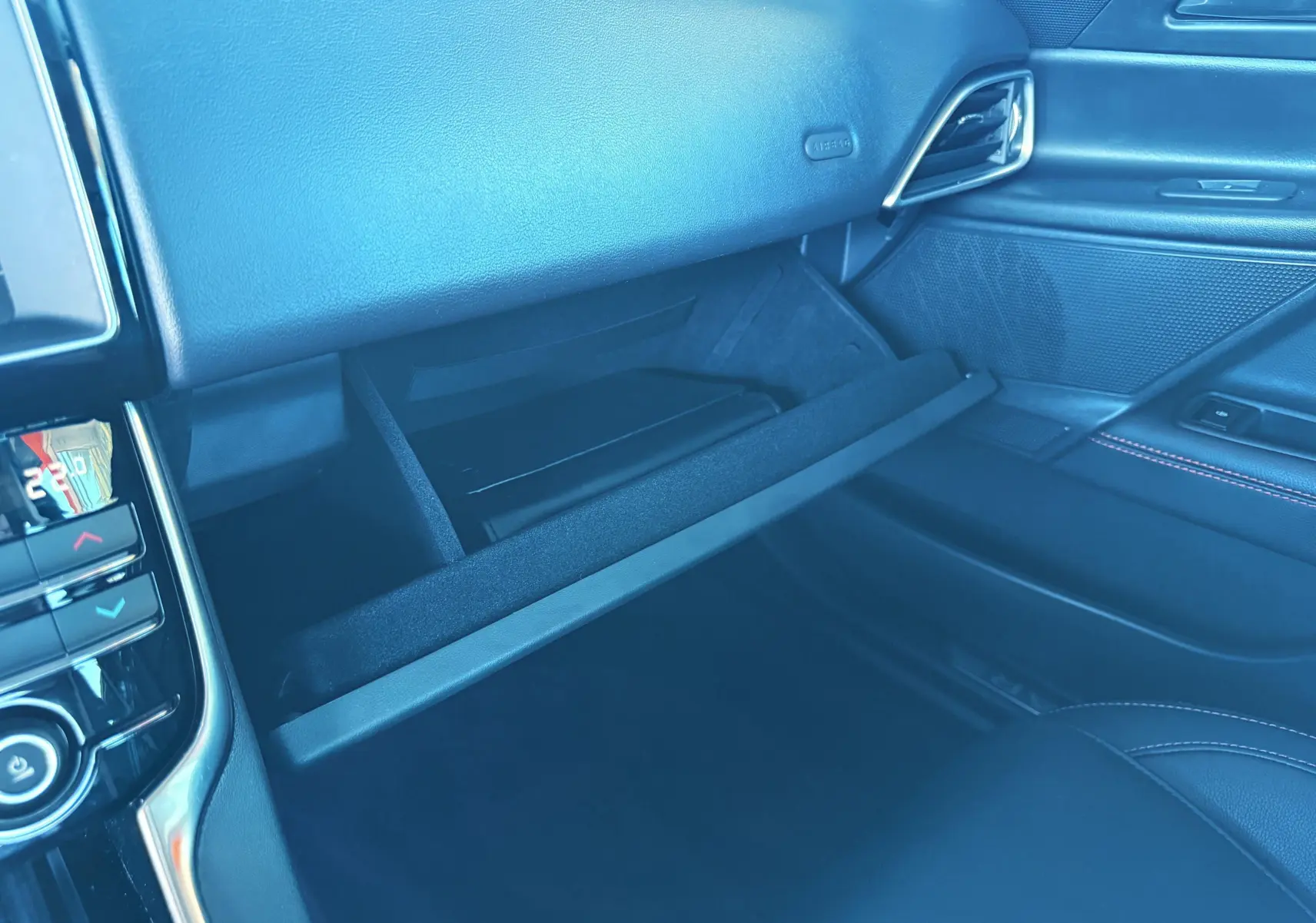 Gros plan sur la boîte à gants ouverte côté passager de la Jaguar XE noire, intérieur cuir noir avec détails chromés.