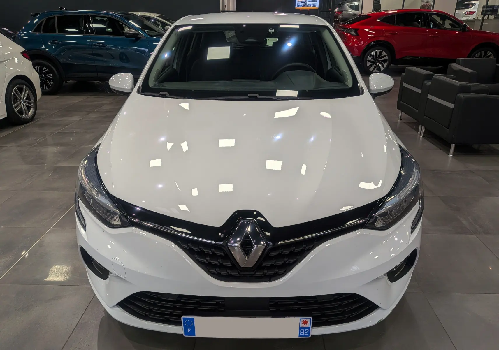 Vue avant d'une Renault Clio V blanche Glacier en showroom, mettant en valeur la calandre noire et les phares modernes.