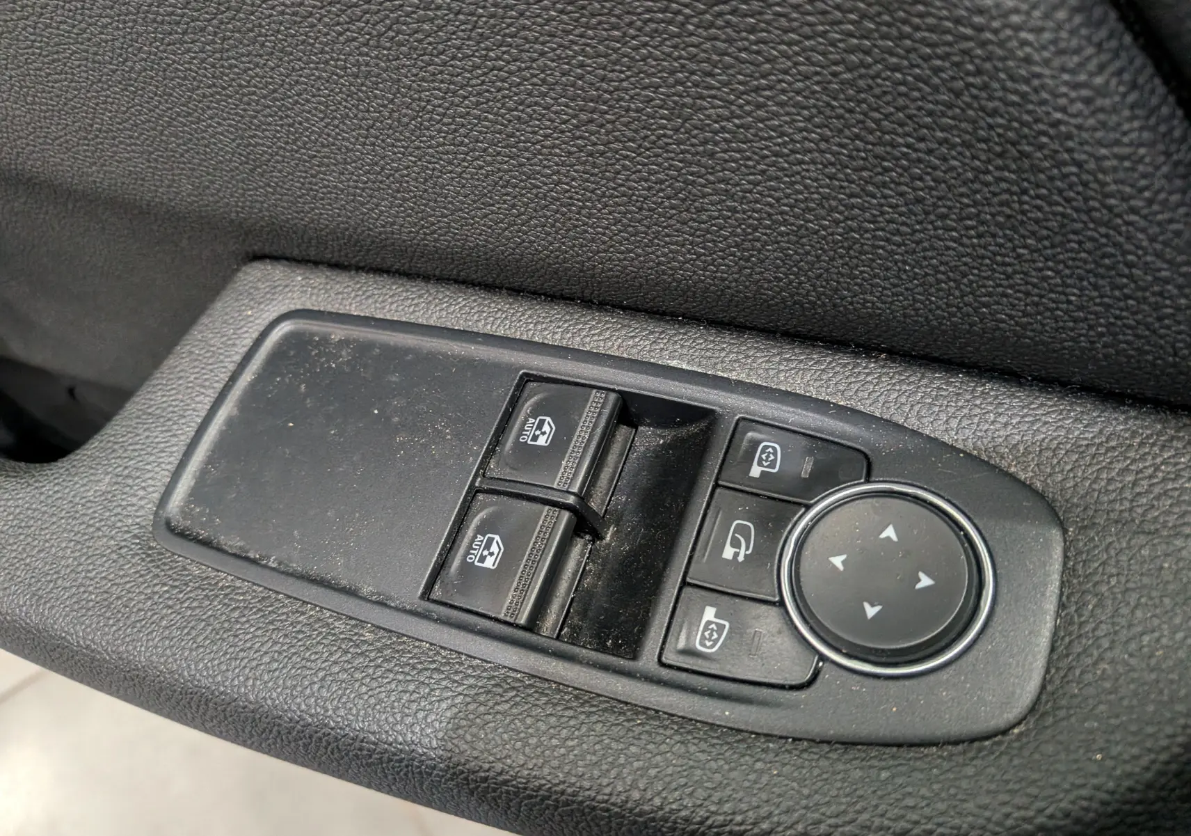 Gros plan sur les commandes de lève-vitres et réglage des rétroviseurs côté gauche d'une Renault Clio V blanche.