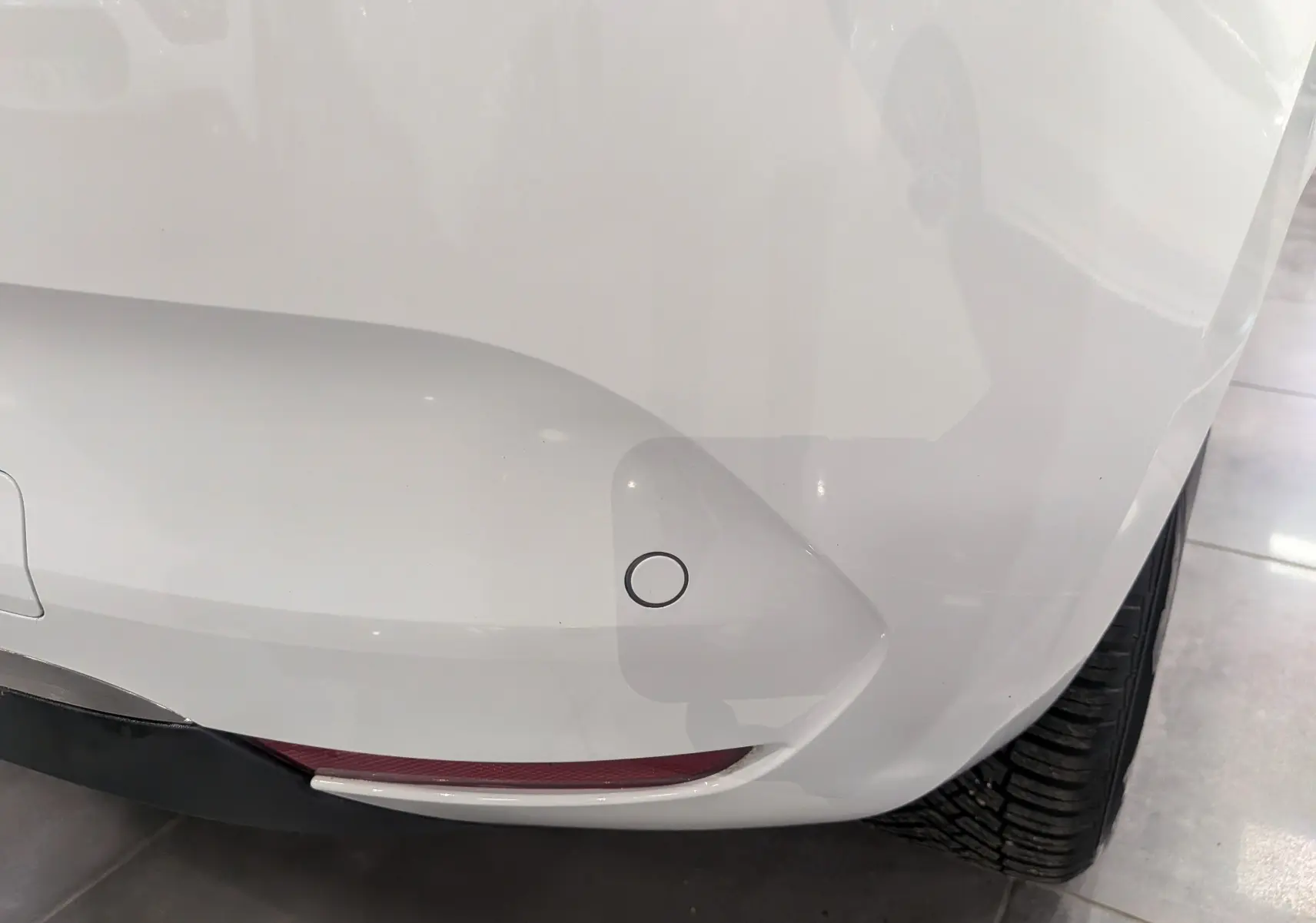 Gros plan sur le pare-chocs arrière droit blanc glacier d'une Renault Clio V TCe 100 CH X-TRONIC BUSINESS avec capteur de recul.